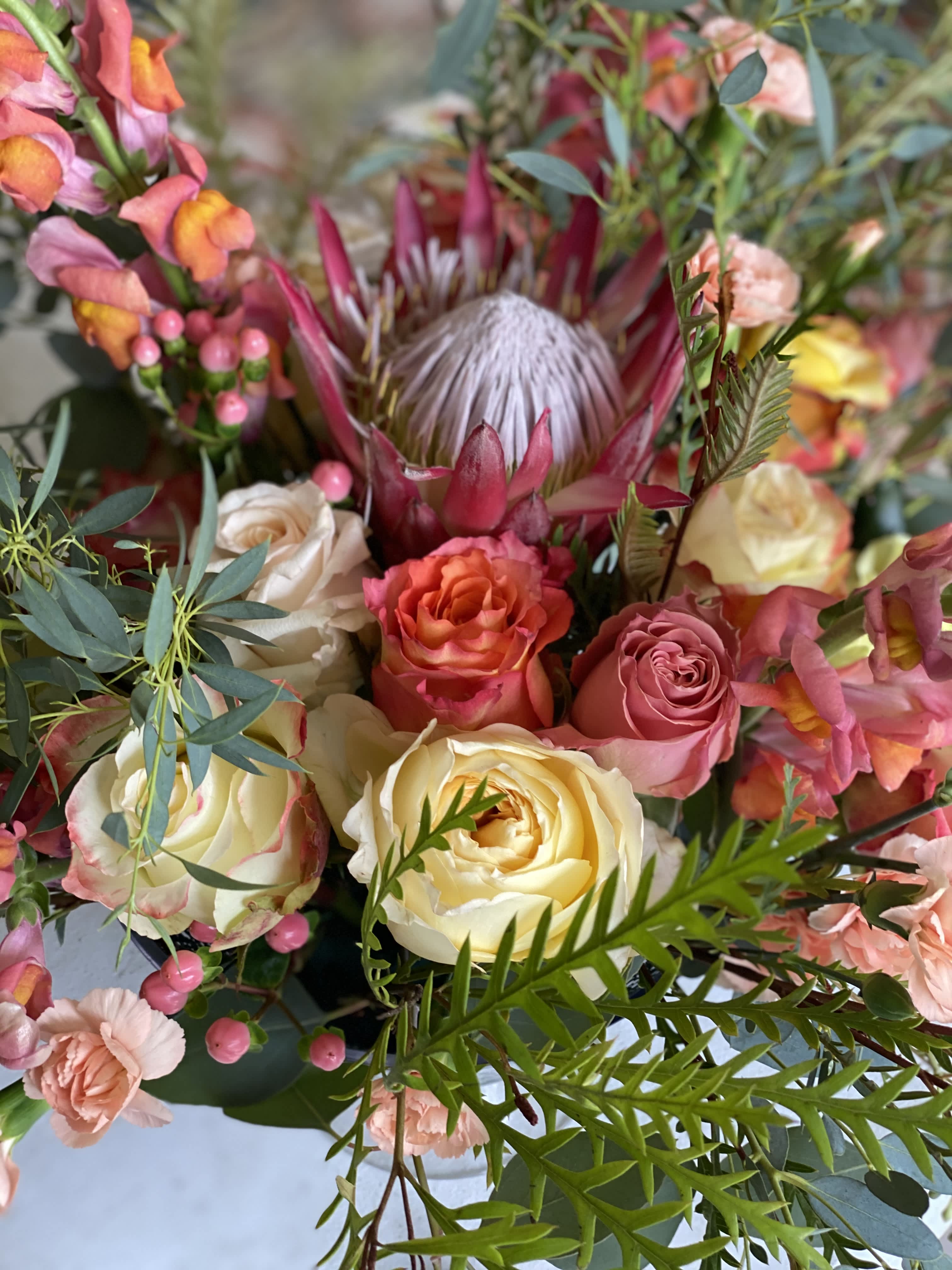  Tuscan Light - This stunning arrangement boasts all the colors and tones of the Italian sunlight, creamy yellows, muted fresh pinks, and tones of terra cotta. The soft roses encompassing the beautiful massive protea gives this arrangement texture and style that is like no other.