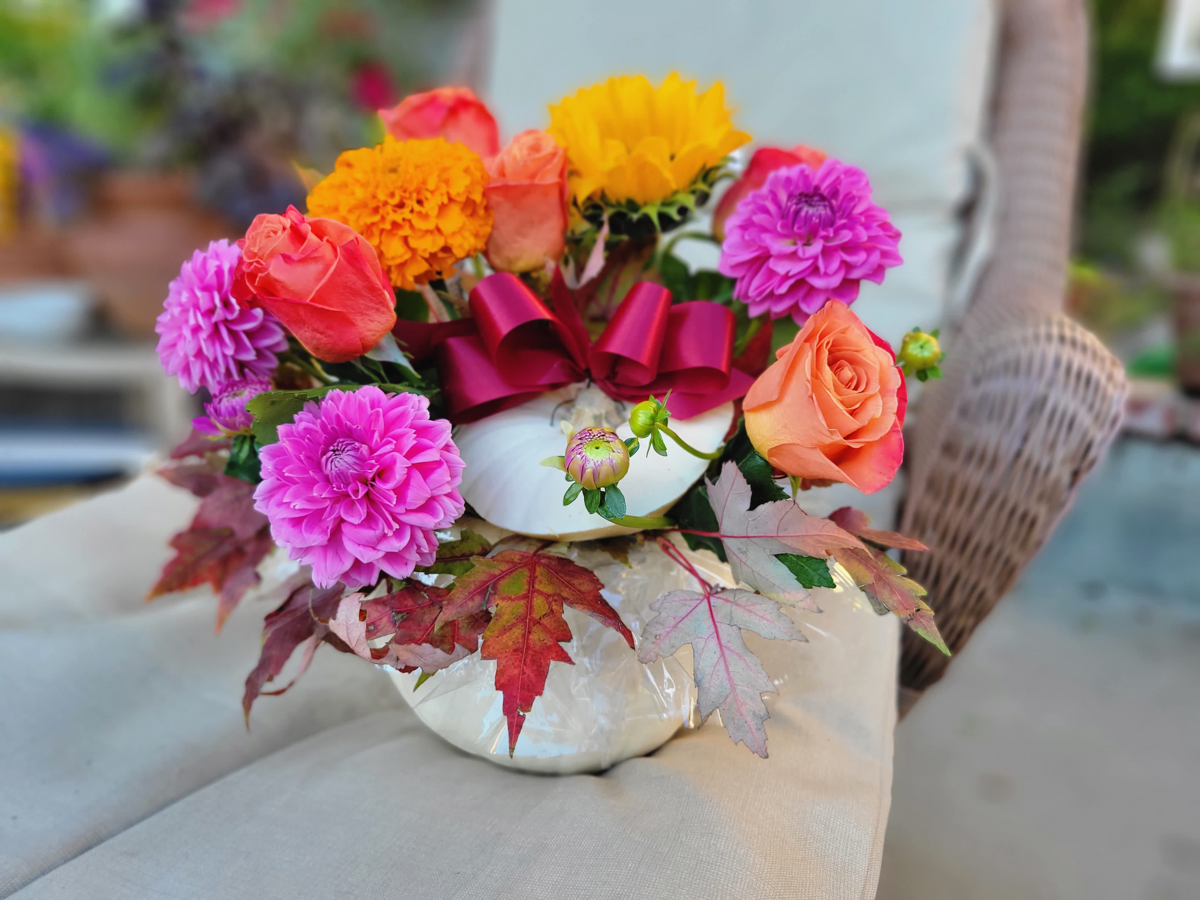 Perfectly Pumpkin Authentic Floral Arrangement - This Autumnal Best Seller is a popular Choice the entire duration of fall! From the classroom in September, to the entry way at Halloween, to the Coffee table at Thanksgiving. This Authentic Pumpkin arrangement never ceases to charm guests and inspire fall feelings when it counts!  This beautiful arrangement features: An Authentic white pumpkin, Orange roses, Dahlias, Sunflowers, &amp; supporting fillers and greens. Appropriate substitutions that may be found in this arrangement are skillfully selected to achieve the ultimate fall look include: Amaranth, Maple leaf, Ranunculus, teddy bear sunflower, red sunflower, marigolds, Hypericum Berry, or various fall colors, yellow, orange, pinks, and reds!  This Arrangement is available late August to Late November!