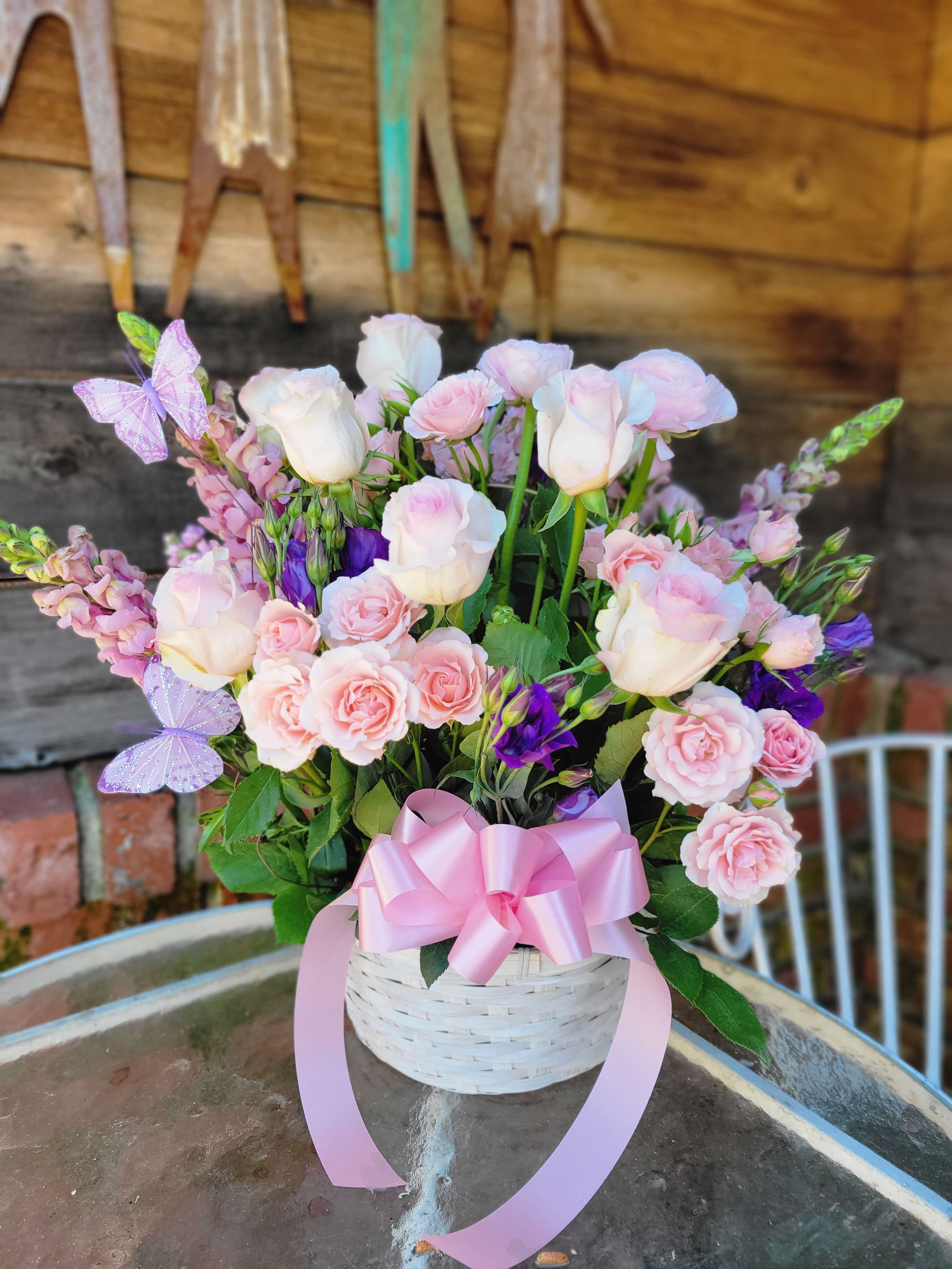 Country Bloom Floral Basket - The Country Bloom Basket is one of our Best Sellers! As it has been a popular choice for Birthday's, Get well, Congratulations, New Baby, and even Anniversary! This arrangements comes in a handled basket, and features: Pink roses, Snap dragons, Spray roses, Butterfly picks, and Supporting florals!  Our standard size is designed around 7 roses in a handled basket Our Deluxe size is designed around 8 roses with an increase of supporting florals in a medium sized basket Our Premium size is designed around 10 roses in a large size basket with an increase of supporting florals