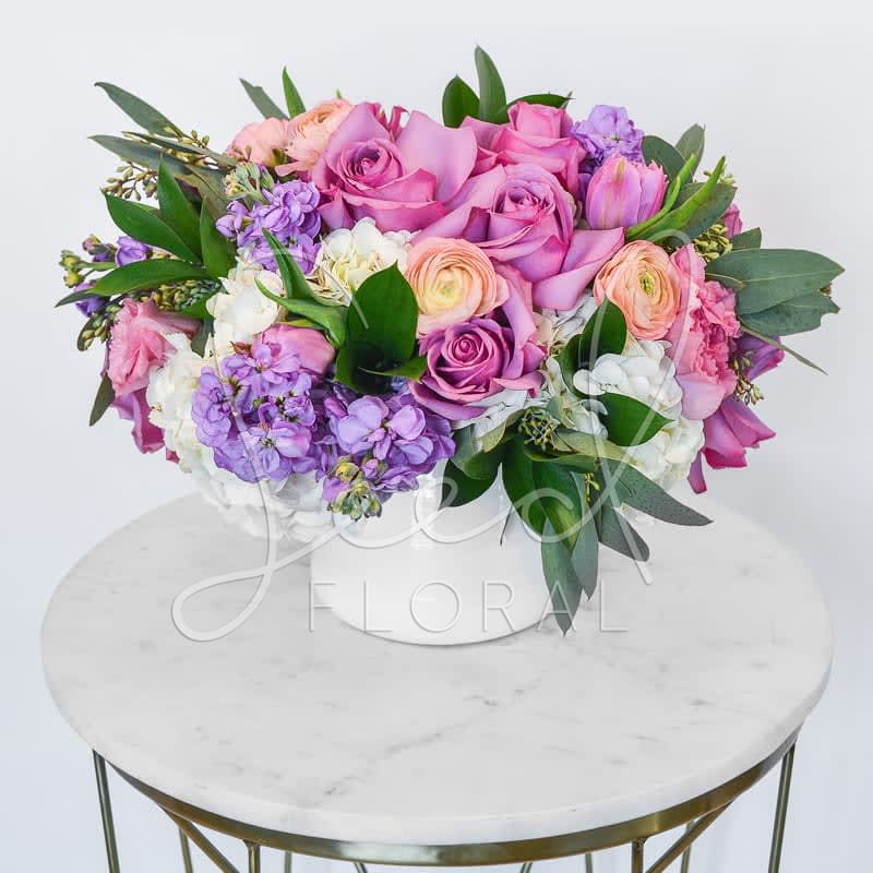 Lavender Class - The name says it all... its classy and chic!   Featuring: Lavender roses, tulips, ranunculus, white hydrangeas and subtle touches of greenery arranged in a white ceramic vase.