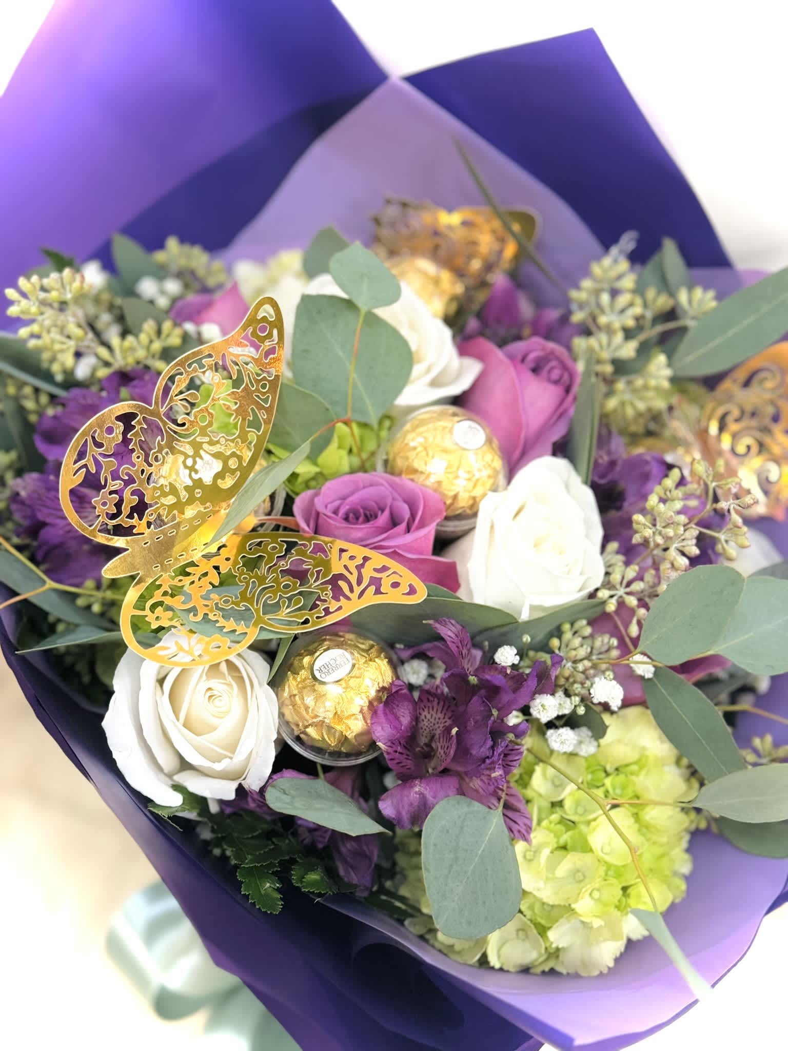 Lavender Whispers: A Symphony of Purple with Foil Butterflies Lavender Whispers: A Symphony of Purple with Foil Butterflies - Indulge in the enchanting allure of our 'Lavender Whispers' Valentine's Day HandWrap. Handcrafted with meticulous care, this exquisite ensemble showcases a harmonious blend of shades of purple and lavender blooms, meticulously wrapped to evoke a sense of timeless elegance. Delicate foil butterflies fluttering gracefully amidst the lush petals, each bloom whispers sentiments of adoration and affection. Perfect for expressing your deepest emotions or surprising a loved one with a touch of ethereal beauty, 'Lavender Whispers' is a true testament to the enchanting power of love. (substitutions may be required. If substitutions are required, arrangement will be similar to photo and will always be in your holiday colors) hand wrap not sold in vase - call if you are looking for other colors thank you!