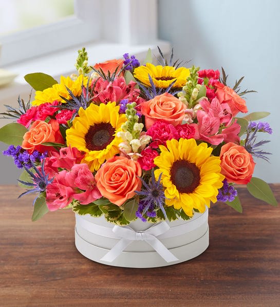 Flower Hatbox - An exquisite gift with beautifully bespoke style. Our vibrant gathering of blooms is arranged in our signature European hatbox: an elegant, new dove gray container finished with a matching ribbon. Its versatile design is perfect for displaying a variety of colors, adding to the custom feeling of this special keepsake.  - All-around arrangement with orange roses, sunflowers, pink snapdragons, hot pink Peruvian lilies (alstroemeria) and mini carnations, blue thistle and purple statice; accented with silver dollar eucalyptus and assorted greenery - Artistically designed in our paperboard hatbox, handsomely wrapped in dove gray with dyed-to-match grosgrain ribbon; water resistant with acrylic liner; do not immerse or leave standing in water; measures 3.5&quot;H x 8.5&quot;W - Our florists hand-design each arrangement, so colors and varieties may vary due to local availability - To ensure lasting beauty, Peruvian lilies may arrive in bud form and will fully bloom over the next few days