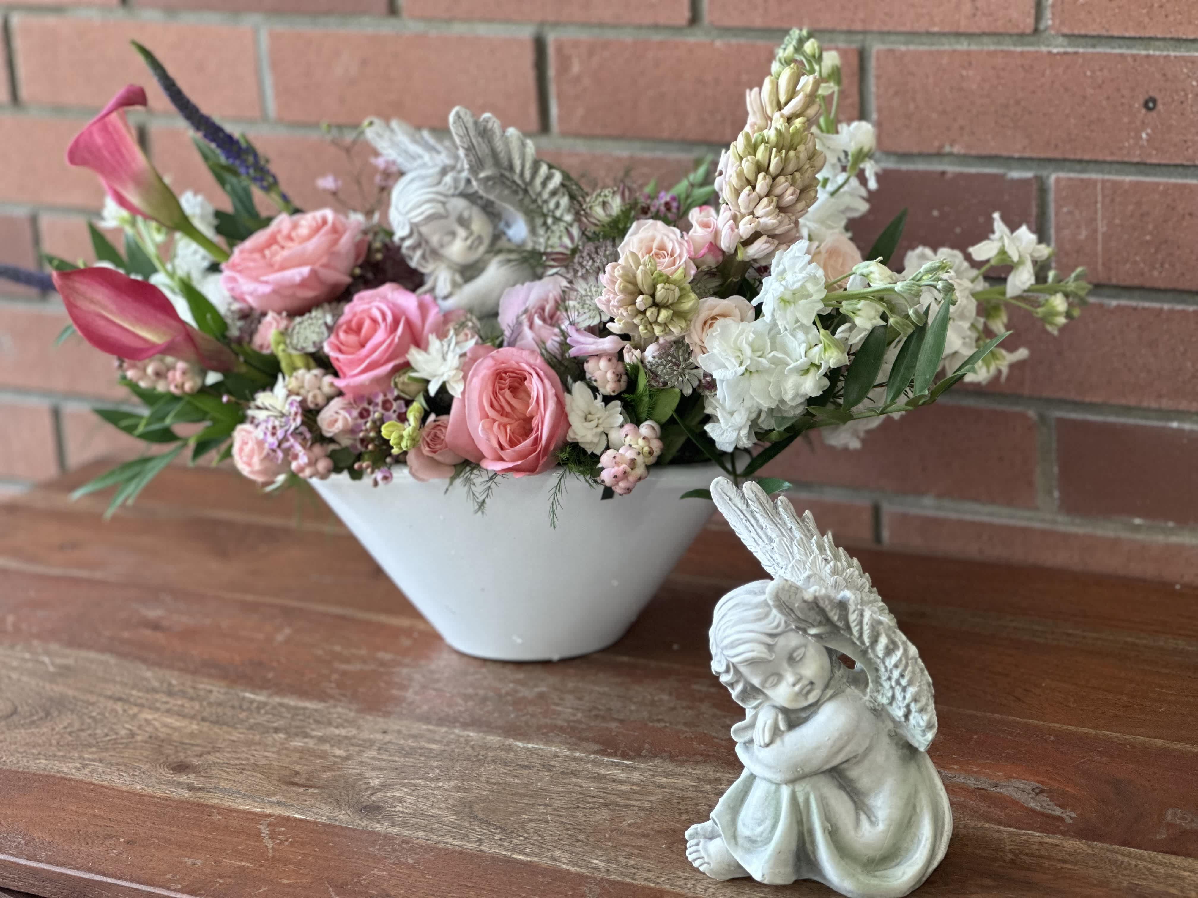 Sleeping Angel Arrangement - Beautiful muted shades of pink and white flowers such as roses, spray roses, hyacinth, mini calla lilies, wax flower, touches of orchids. Eucalyptus and greenery in a beautiful ceramic vase. 8 inch angel statue included in the bouquet.  - deluxe and premium will get $20 or $40 dollars worth of additional fresh cut flowers added to make the size fuller and slightly bigger. 