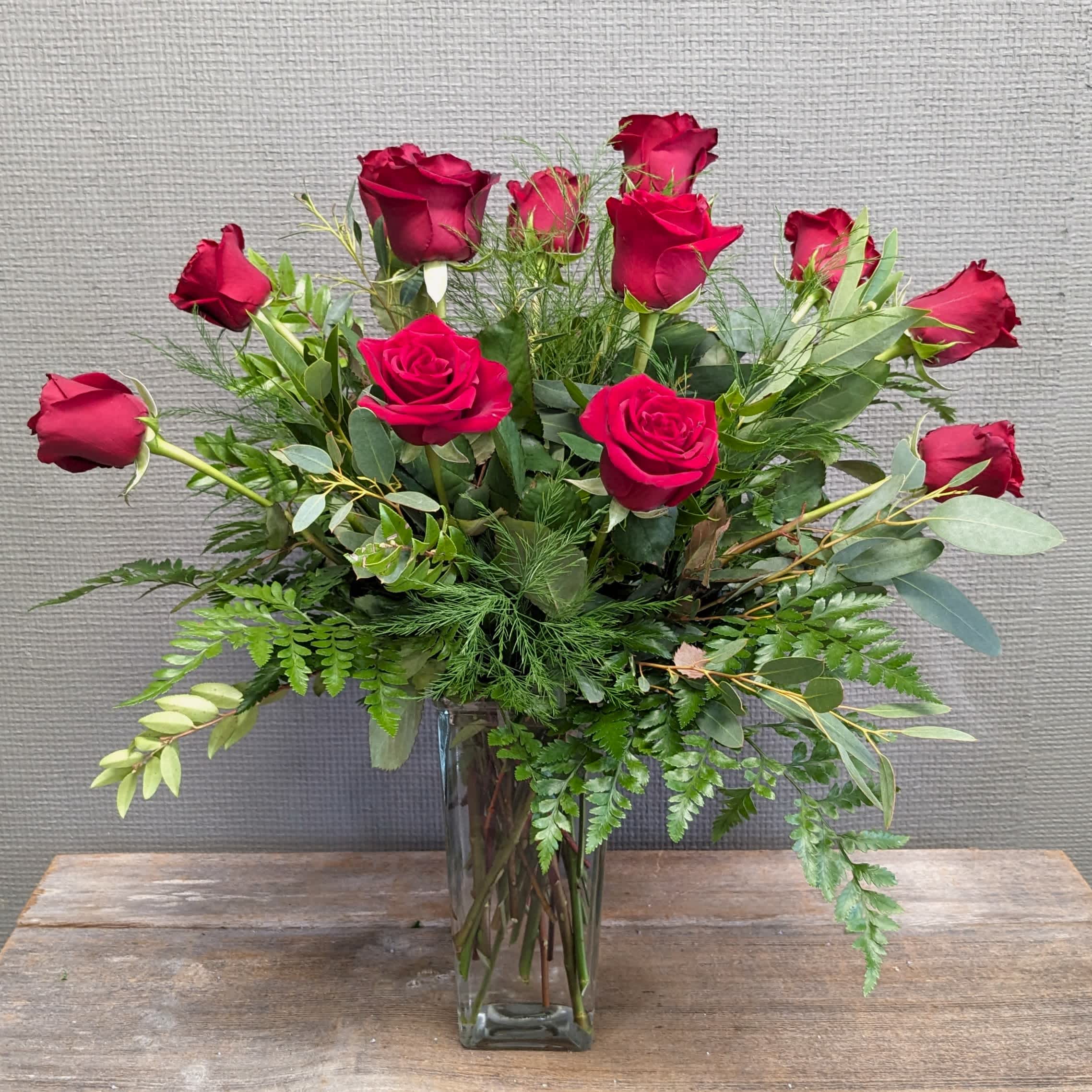 Just Amore - One dozen roses with a mix of only greenery to complement the roses, no filler. Simple and refined, this arrangement lets the natural beauty of the roses take center stage. Deluxe and Premium  upgrades will have 18 and 24 roses respectively. Please let us know in special instructions if you have rose color request other than red; red will be the default.