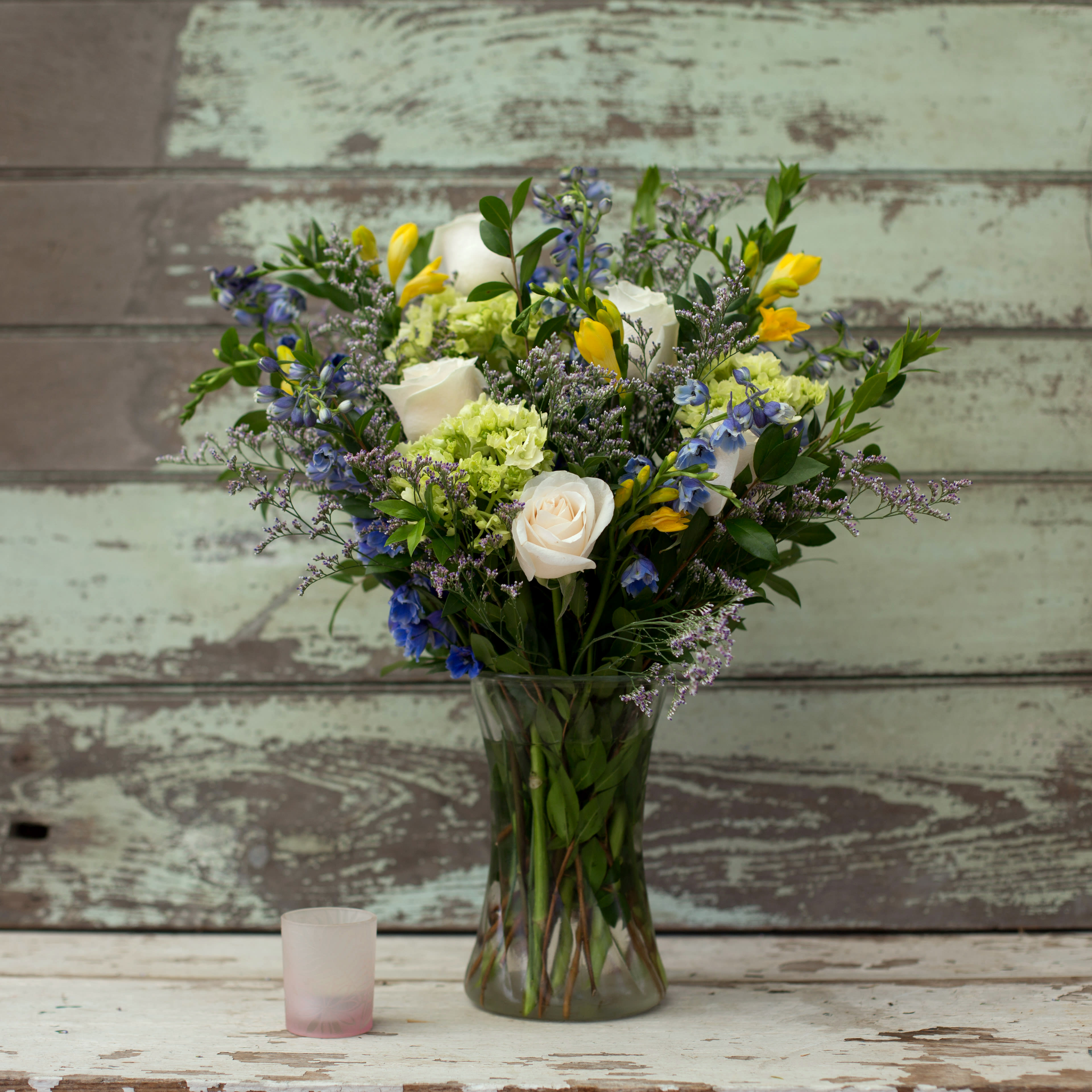 Tiny Treasures - It’s time to celebrate a new life! This gorgeous arrangement will say congratulations in a grand way at home or the hospital. Lovely white/pink roses, yellow freesia, green hydrangea, white/blue delphinium, limonium, and greenery in a clear vase can be personalized to the gender of the baby. We will even use a color appropriate bow!     *Pictured arrangement is for a Baby Boy. Please specify Baby Gender in instructional area.  