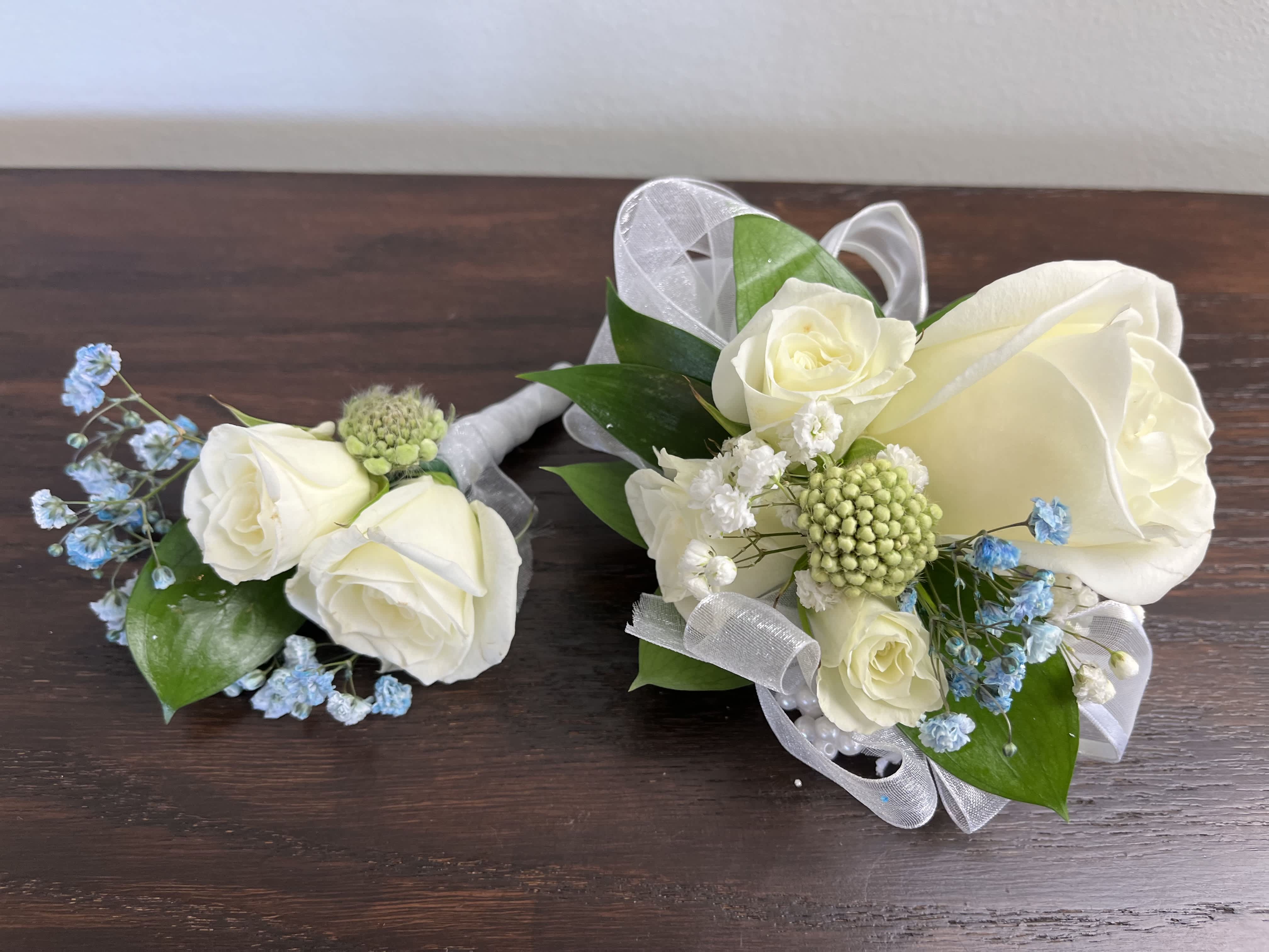 Frosted Elegance 1 Frosted Elegance 1 - Elegant white roses with blue baby's breath and mixed greens. This is a two piece set including one corsage and one boutonniere. Ribbon, wristlets, and colors can be customizable upon request.
