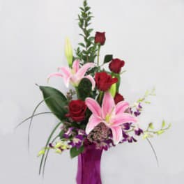 Mother's Love Bouquet - M14 - Red roses, lillies, PURPLE dendrobeum orchids, wax flower artistically arranged in a purple/pink square glass vase accented with ti-leaves, myrtle, lilly grass and salal. Components may vary Vase color may vary