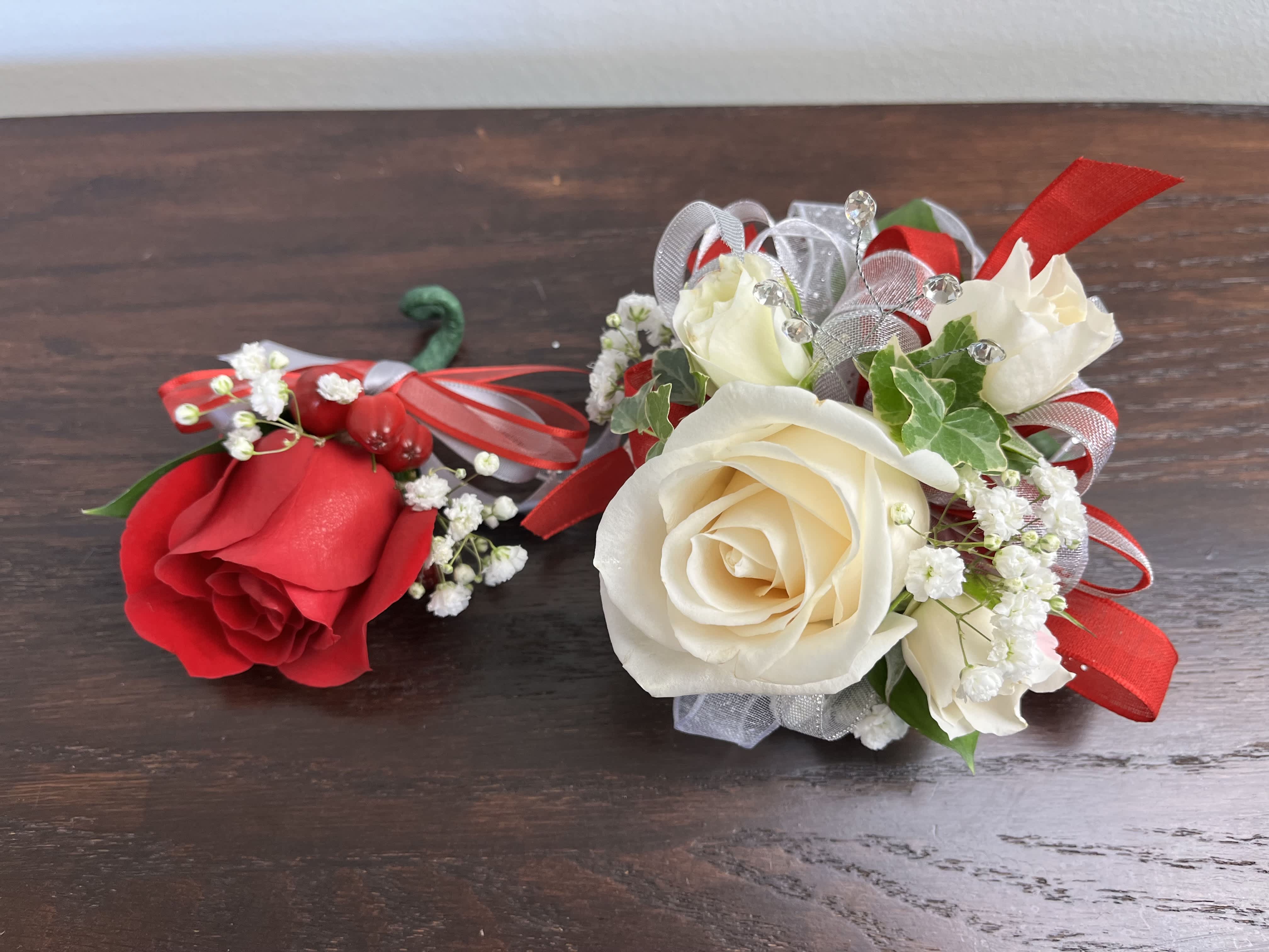 Classic Red - A classic and stunning design featuring red roses, white roses, and baby's breath with mixed greens. This is a two piece set including one corsage and one boutonniere.  Ribbon, wristlets, and colors can be customizable upon request. 
