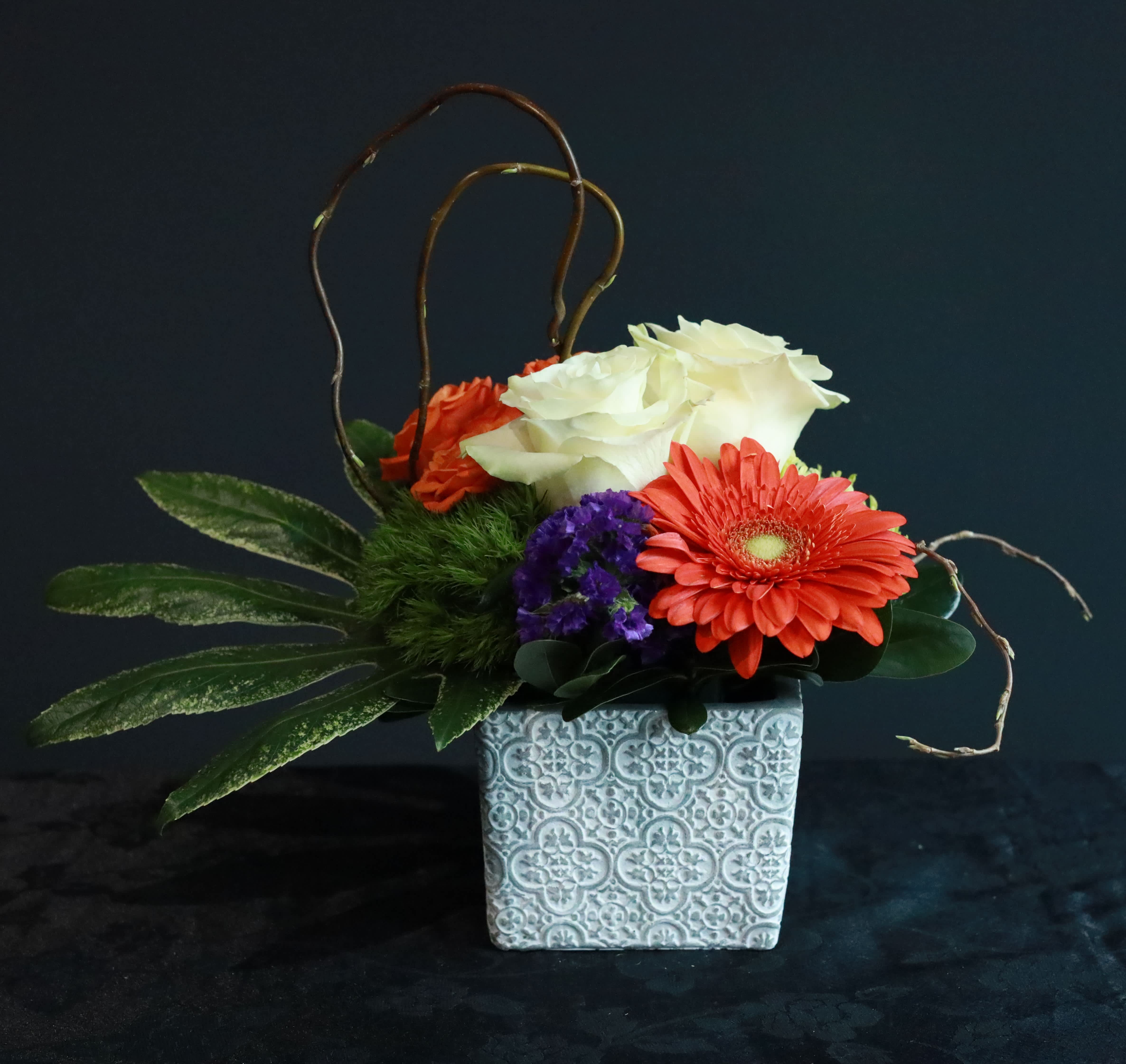 Mosaic Memories - This small sympathy arrangement is a vibrant and uplifting in a unique cube container with a repeating vintage pattern. This cheerful tribute celebrates the life of your loved one with a dazzling mosaic of colorful blooms.