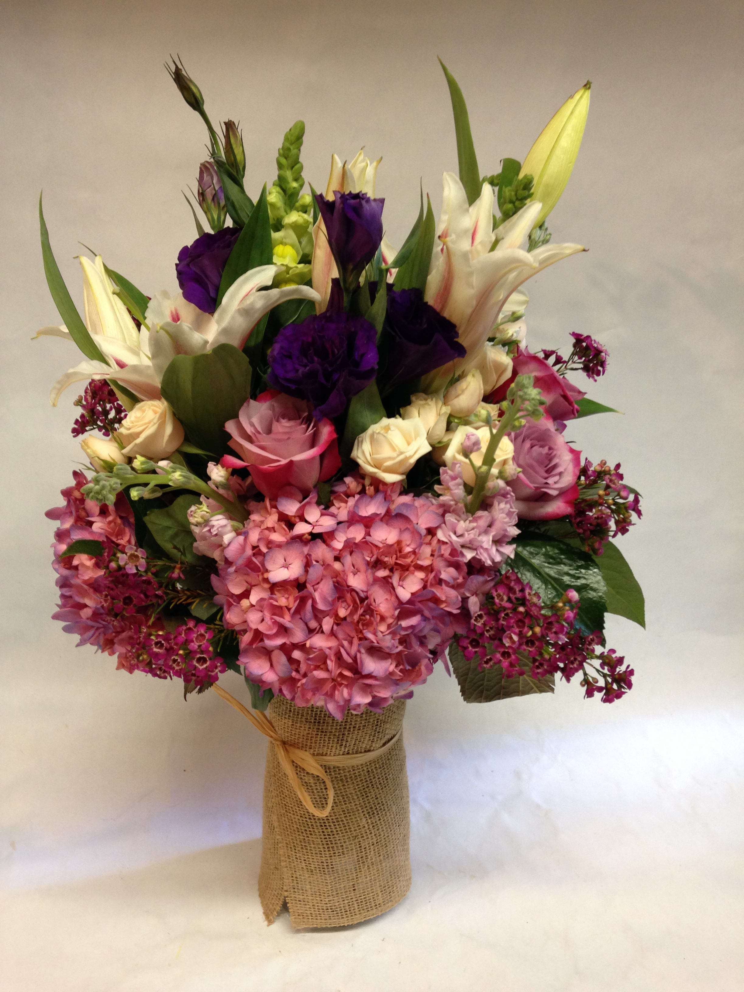 Sweetness - This medium sized arrangement comes complete with lavender hydrangea, casa blanca lilies, deep purple roses, lavender stock, lavender lisianthus, spray roses, snapdragons and wax flower.  (Some flowers may be subject to change depending on the season. We will contact you with available flower substitutions; please contact us with specific questions if you are concerned with flower availability, thanks!) FEATURED ARRANGEMENT: $350,00 (Regular Price))