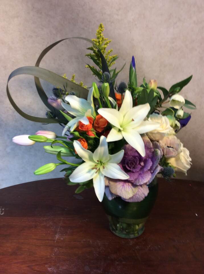 Kale Garden Collection - Our Collection of Garden flowers include Iris, Roses, Lilies, Tulips, Helbores, Thistle (Eryngium) With Kale as a focal point. New Zealand Flax Fashioned into a modified Heart adds line a motion to this stately center piece arrangement.