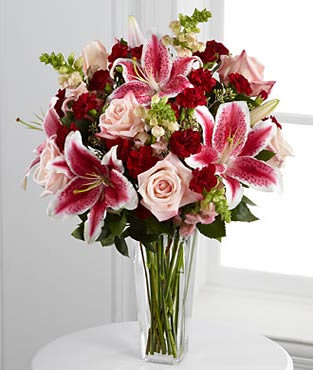 More than Love - Sweetly sophisticated and bursting with soft sentiments to sweep them off their feet. Pale pink roses, Stargazer Lilies, burgundy mini carnations, dark pink snapdragons and lush greens are gorgeously arranged in a square tapered clear glass. 