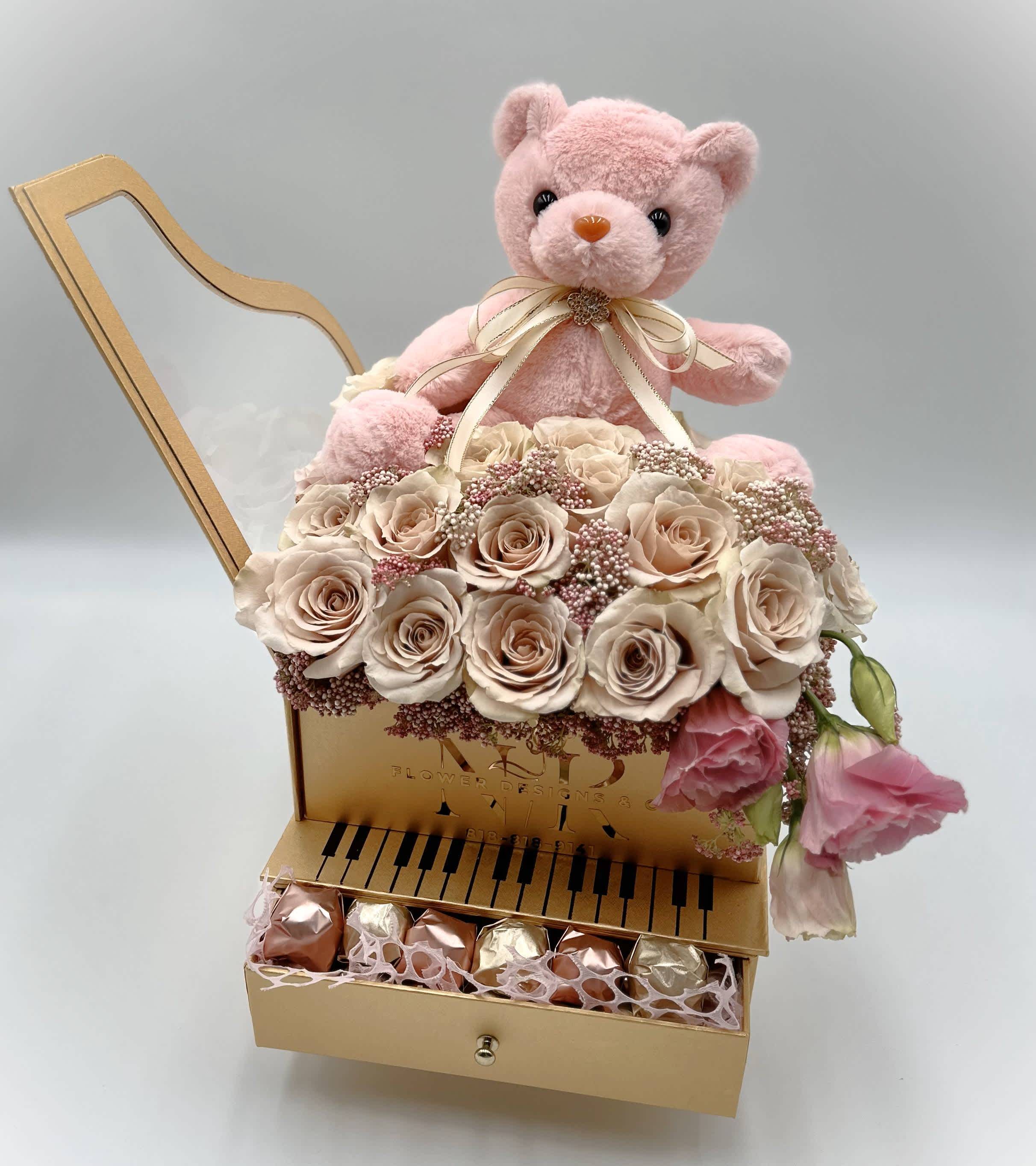 Baby Girl Piano - Tasteful way to welcome a baby girl! Soft pink roses with a teddy bear, wearing a bow with a crystal accent in a piano box. Flower and Chocolates in One! Standard box comes with Ferrero Roche chocolates. Premium options can be customized.