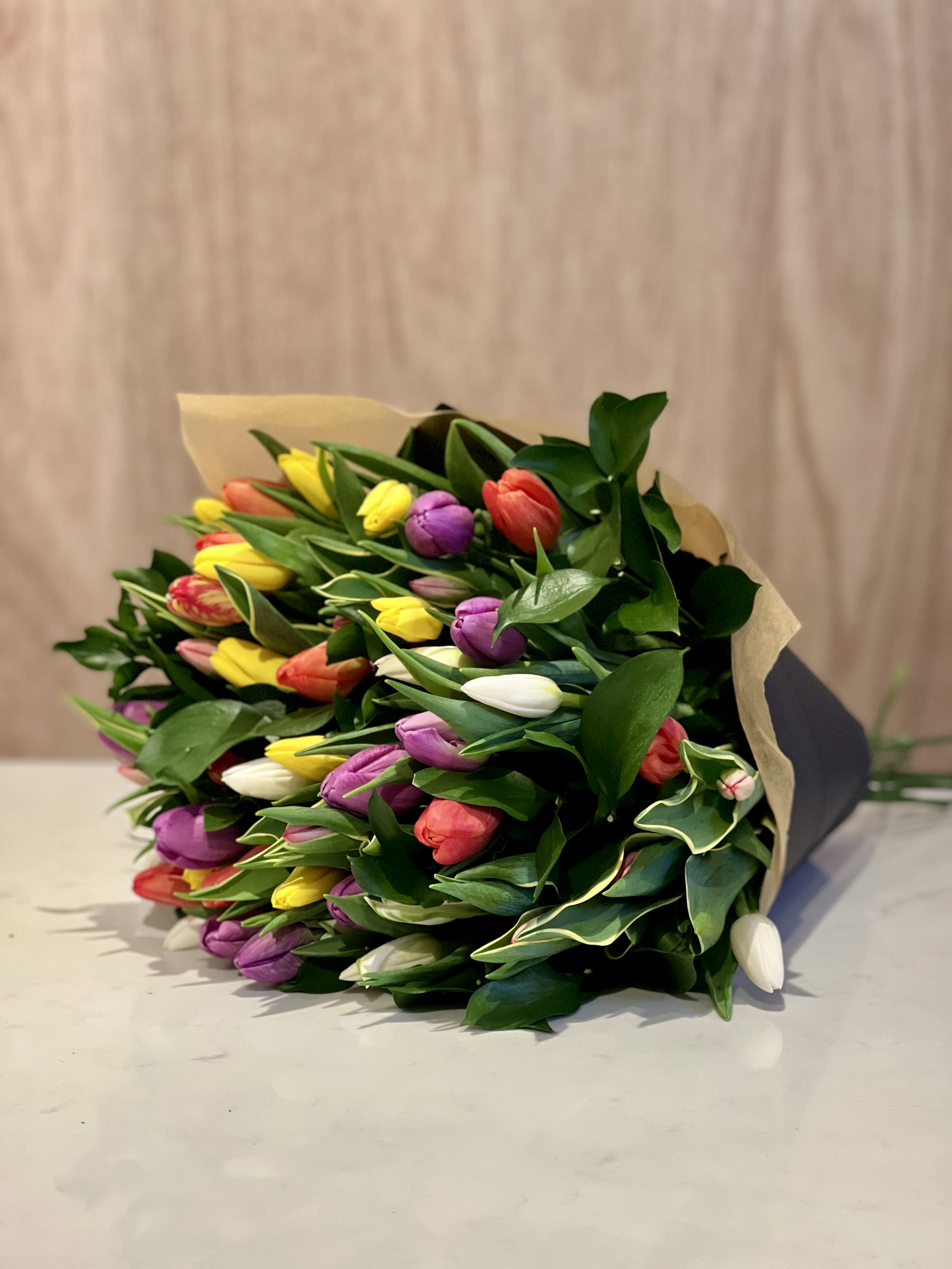 TULIP BOUQUET - Radiating vibrant charm, this beautiful bouquet spotlights a collection of tulips thoughtfully gathered in a delightful array of sizes and hues. Hand-wrapped and finished with ribbon, this bouquet emanates a lively and spirited aesthetic.