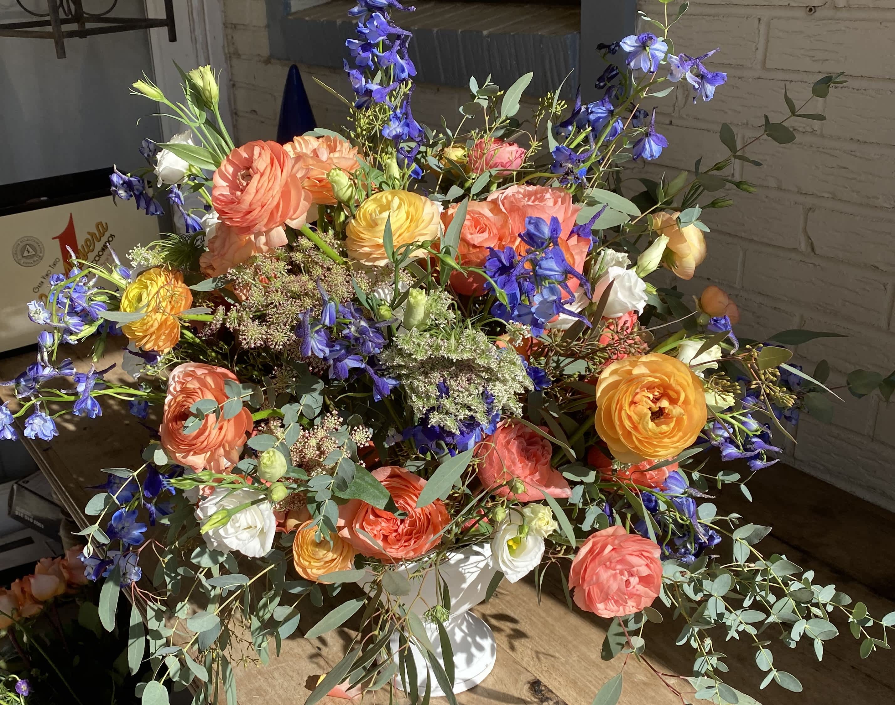 Peachy Keen - This arrangement is a joy to behold with its peach tones, deep blues, and eucalyptus cascading in every direction. The delicate round ranunculus and Garden Roses give this arrangement a soft and rounded feel, while the seeded eucalyptus and blue delphinium add interest, depth, and texture.