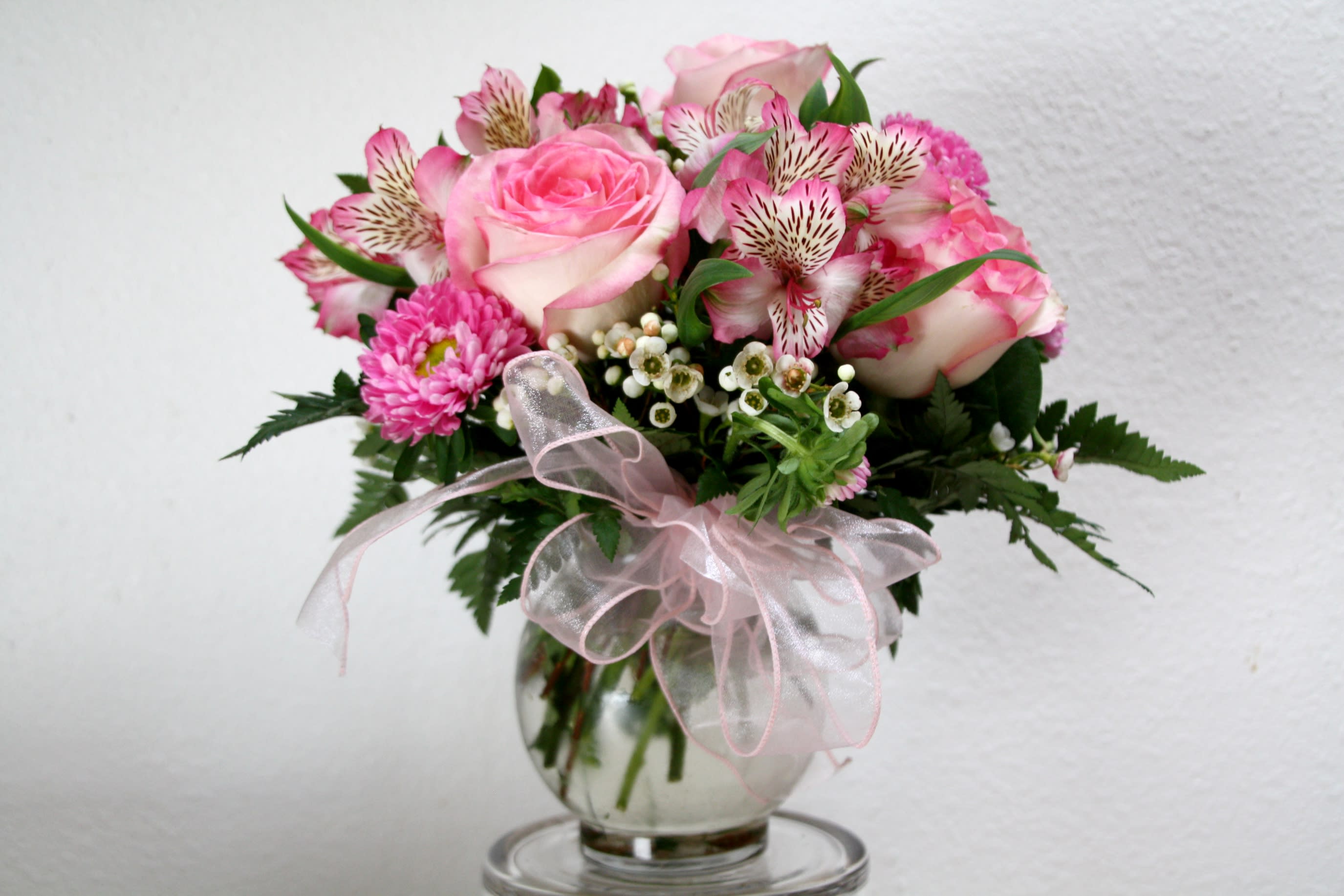 Soft-Spoken - This beautiful arrangement comes with light pink roses, pink alstromeria, and pink asters. It’s accented with waxflower and comes in a clear glass vase and complete with a matching bow. The perfect gift for this Valentine’s Day!