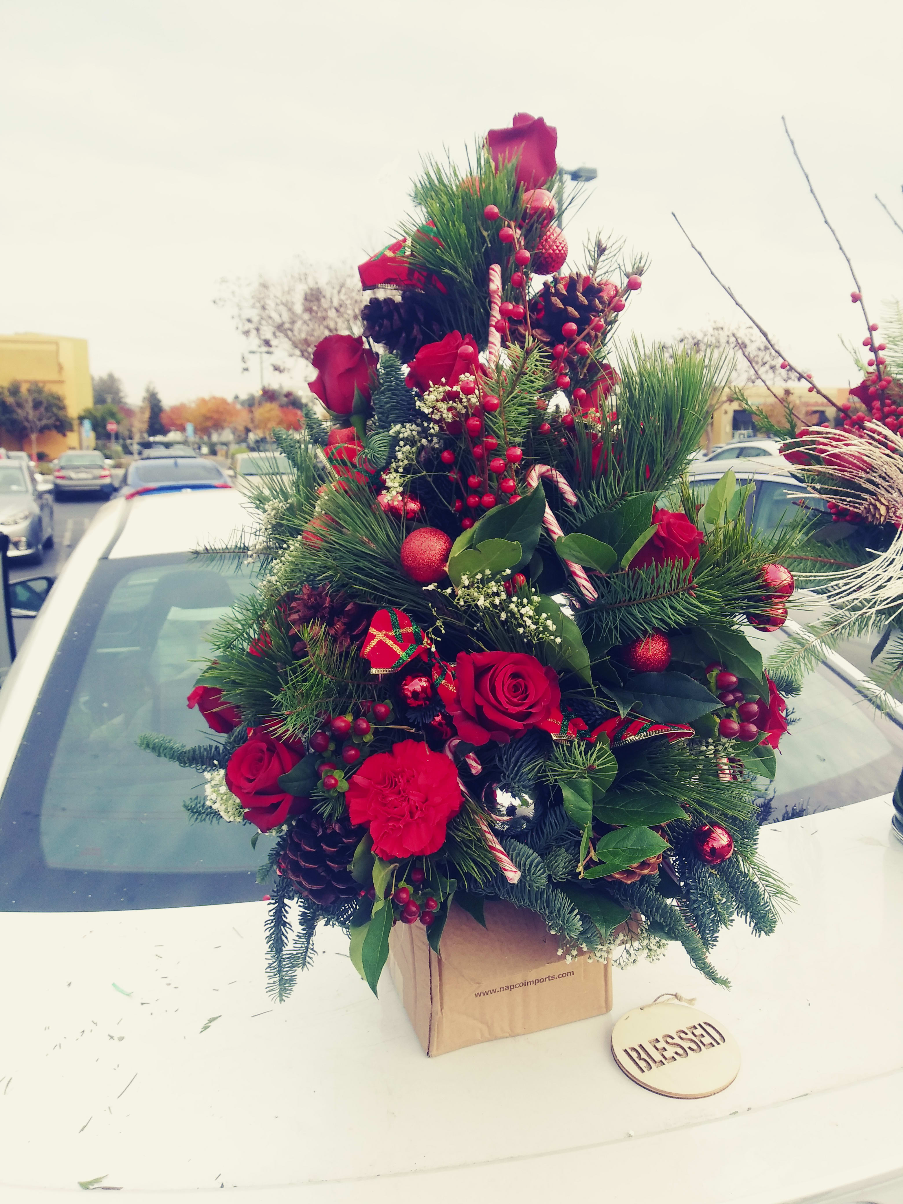 Christmas Tree Christmas Tree - This flower creation leaves nothing to the imagination. The perfect gift of the traditional Christmas tree with ornaments, candy canes and more. Finished off with the kiss of red roses and carnations to becomes the perfect center peiece for your holiday festivities.