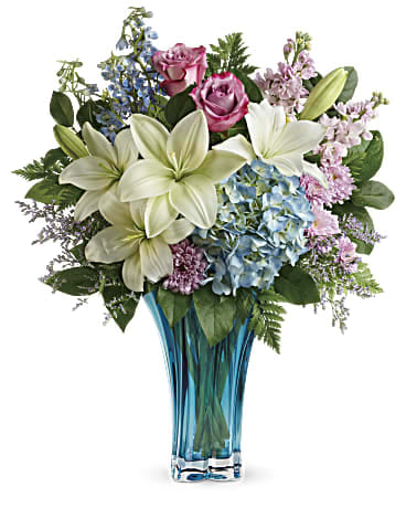 Teleflora's Heart's Pirouette Bouquet - Make mom's heart do pirouettes! Nothing spoils her on Mother's Day like a grand bouquet of hydrangea and roses, artistically arranged in this awe-inspiring, azure blown glass vase. This arrangement features blue hydrangea, lavender roses, white asiatic lilies, light blue delphinium, light pink stock, lavender cushion spray chrysanthemums, misty blue limonium, leatherleaf fern, and lemon leaf. Delivered in Teleflora's Heart's Pirouette vase. Orientation: One-Sided
