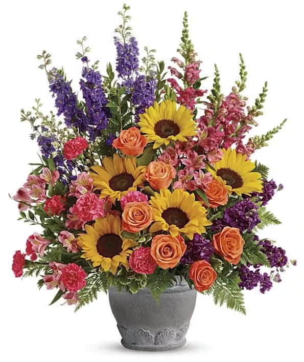 JOY - Send a message of warmth and hope with this magnificent display of sunflowers and roses in a large antiqued pot, a colorful tribute that will warm their hearts.  This bright arrangement includes orange roses, pink alstroemeria, hot pink carnations, yellow sunflowers, purple larkspur, purple stock, hot pink snapdragons, myrtle, variegated pittosporum, and leatherleaf fern.