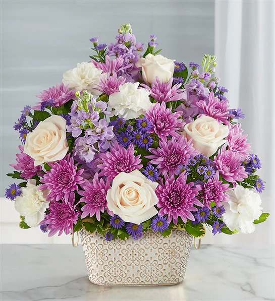 Loving Remembrance  Lavender and White - Celebrate the life of a loved one with our beautiful floral tribute. A mix of blooms in soothing shades is a symbol of enduring love. Designed in our Remembrance Cachepot, featuring an embossed pattern and finished with a gold brushed ivory surface.