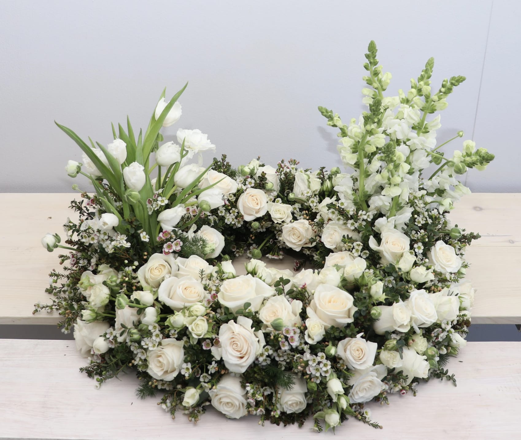 Urn Wreath in Whites  - This urn tribute wreath includes a mix of flowers, roses, and seasonal greens. In the special instruction let us know what colors you would like. Standard size is 30'', deluxe is 36'' and premium is 42''. Interior diameter is about 10'' for standard size.