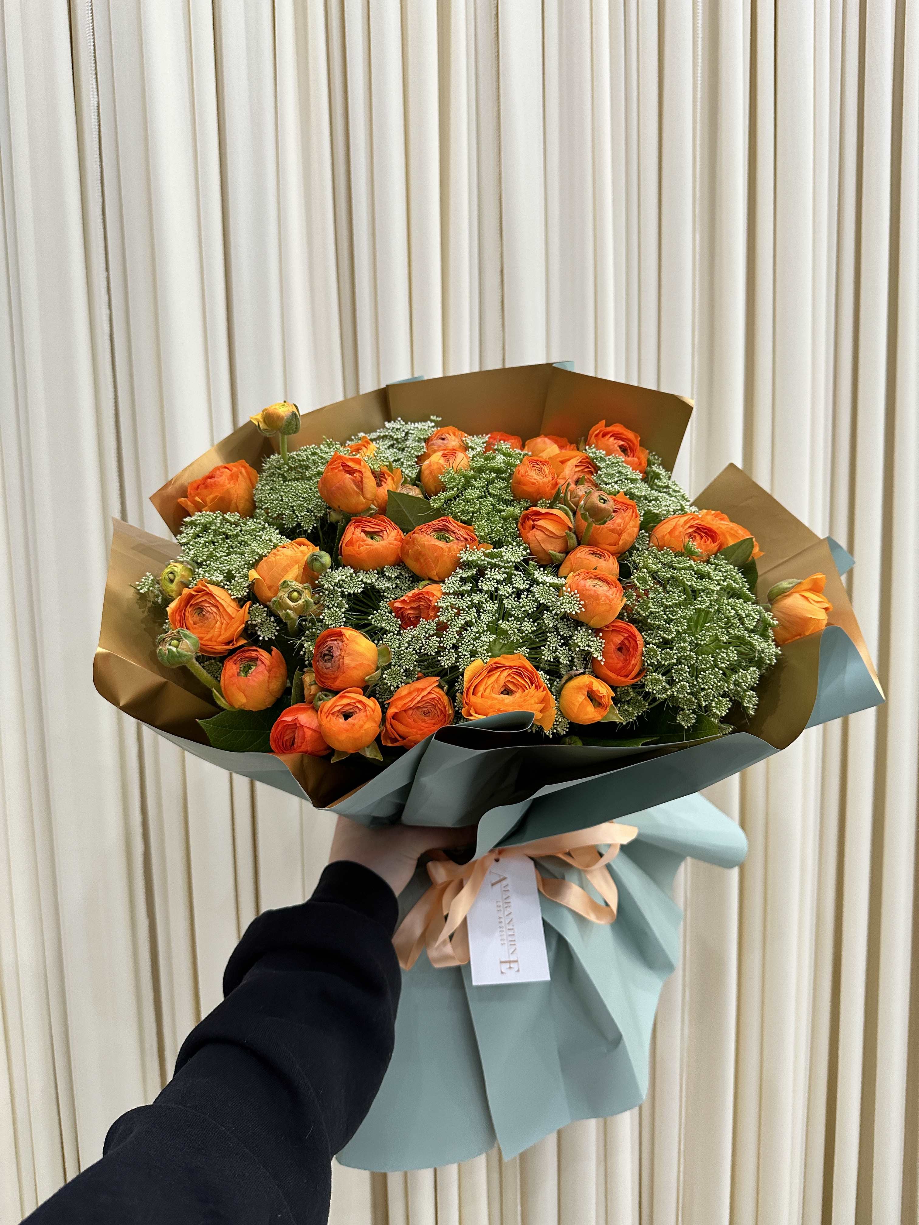 Citrus Splash - This vibrant bouquet bursts with sunshiney orange ranunculus blooms, accented with wispy green mist for a touch of whimsy. The cheerful orange flowers are guaranteed to brighten any day, while the soft green mist adds a touch of elegance and intrigue.
