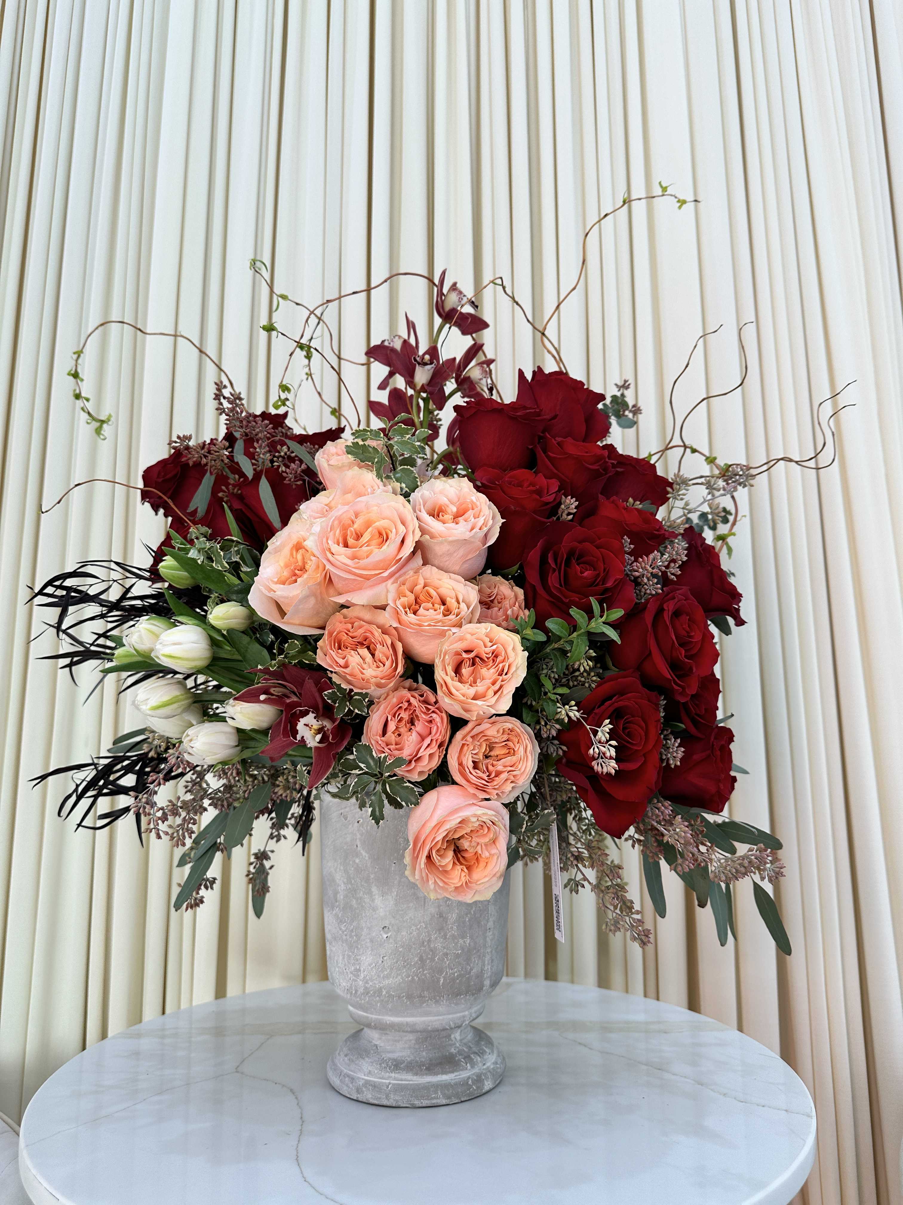 Vibrant Harmony - This captivating arrangement showcases a stunning harmony of color and texture. Rich red roses symbolize love and passion, while the vibrant tulips add a touch of cheerfulness. Delicate cymbidium orchids provide a touch of elegance, and lush greenery completes the arrangement, creating a truly unforgettable gift.