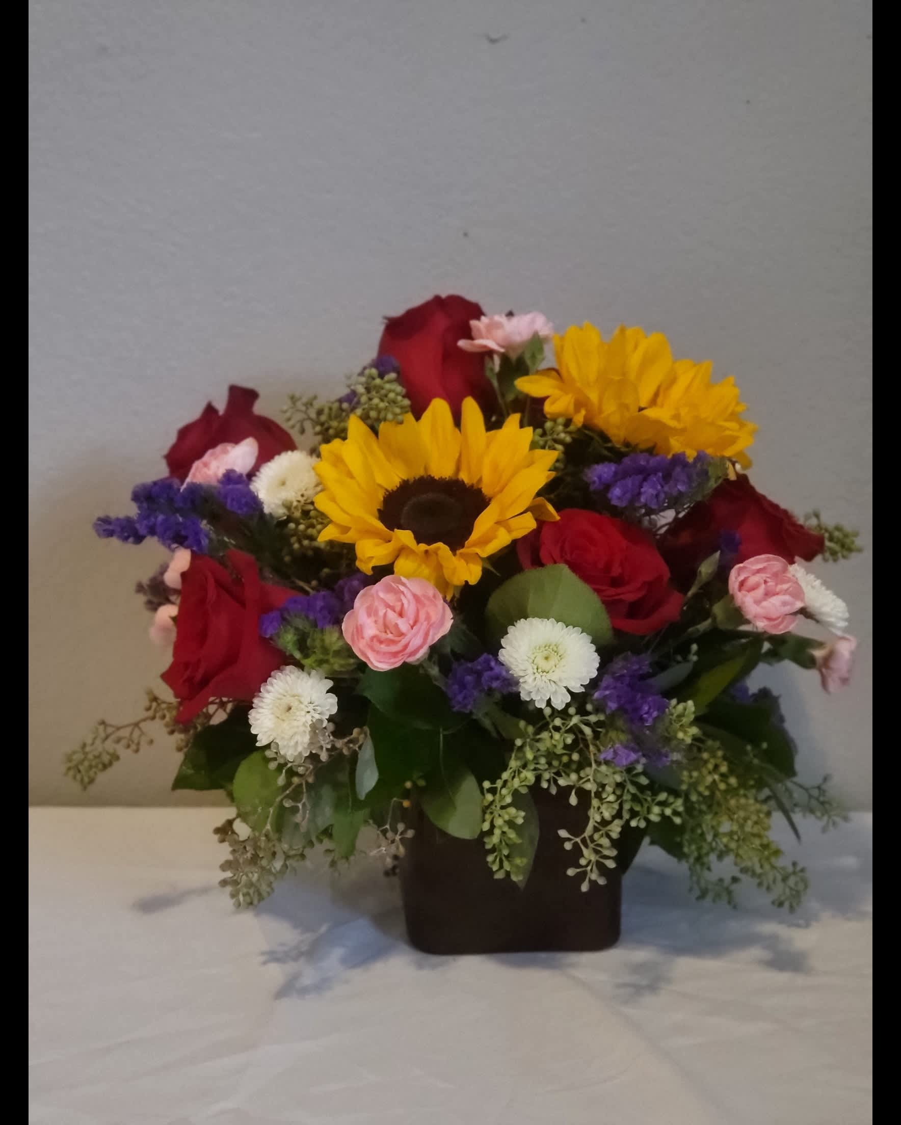 Sunny Rose Cube Special - Lovely Sunflowers mixed with the most stunning red roses accompanied by luscious poms, mini-carnations, and assortment of greens in our perfectly sized red cube.  Great for all occasions! 