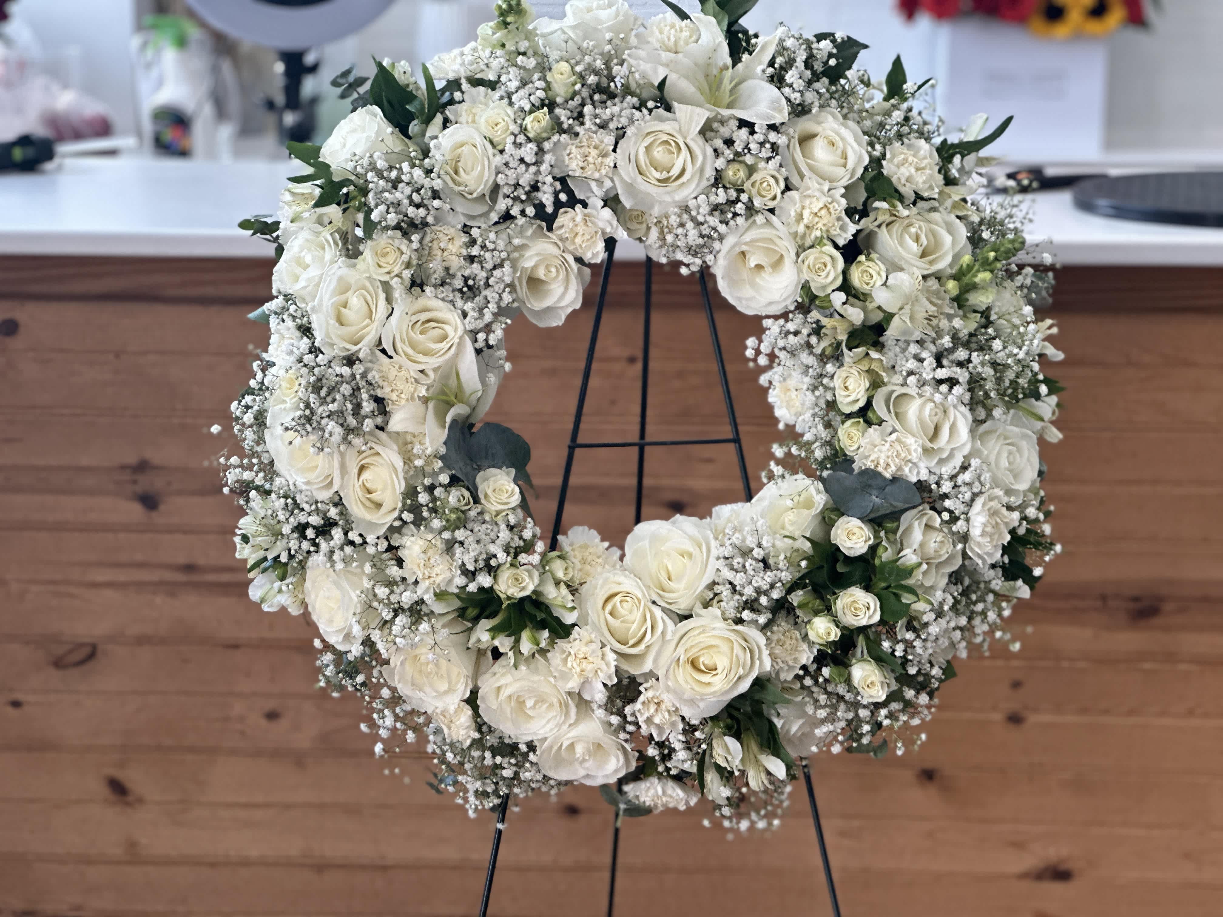Blanc Femme Memorial Wreath - Introducing the &quot;Blanc Femme Memorial Wreath,&quot; a round wreath composed entirely of white flowers, symbolizing purity and reverence.  Experience the timeless elegance of our Blanc Femme Memorial Wreath, a graceful tribute designed to convey honor and respect during remembrance.  Order now to commemorate with dignity and grace through this beautiful floral arrangement.