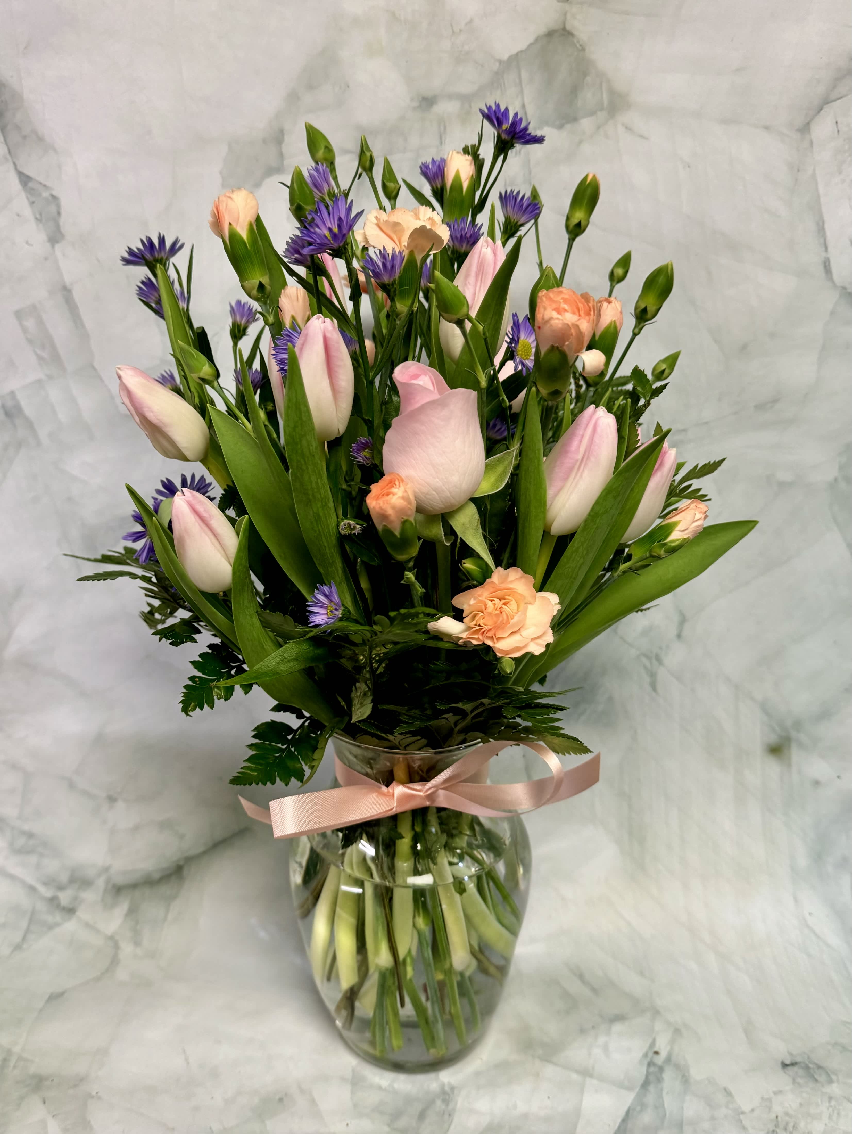 Pink, Peach and Purple Perfection - This arrangement includes the three P’s; pink, purple and peach! These words don’t just have their first initial in common, but they are also three of the most popular colors for flowers. These soft shades are perfect for any occasion. This arrangement includes everyone’s favorite, Roses and also timeless tulips. The filler that is used is wild purple aster and long lasting Mini Carnations. 