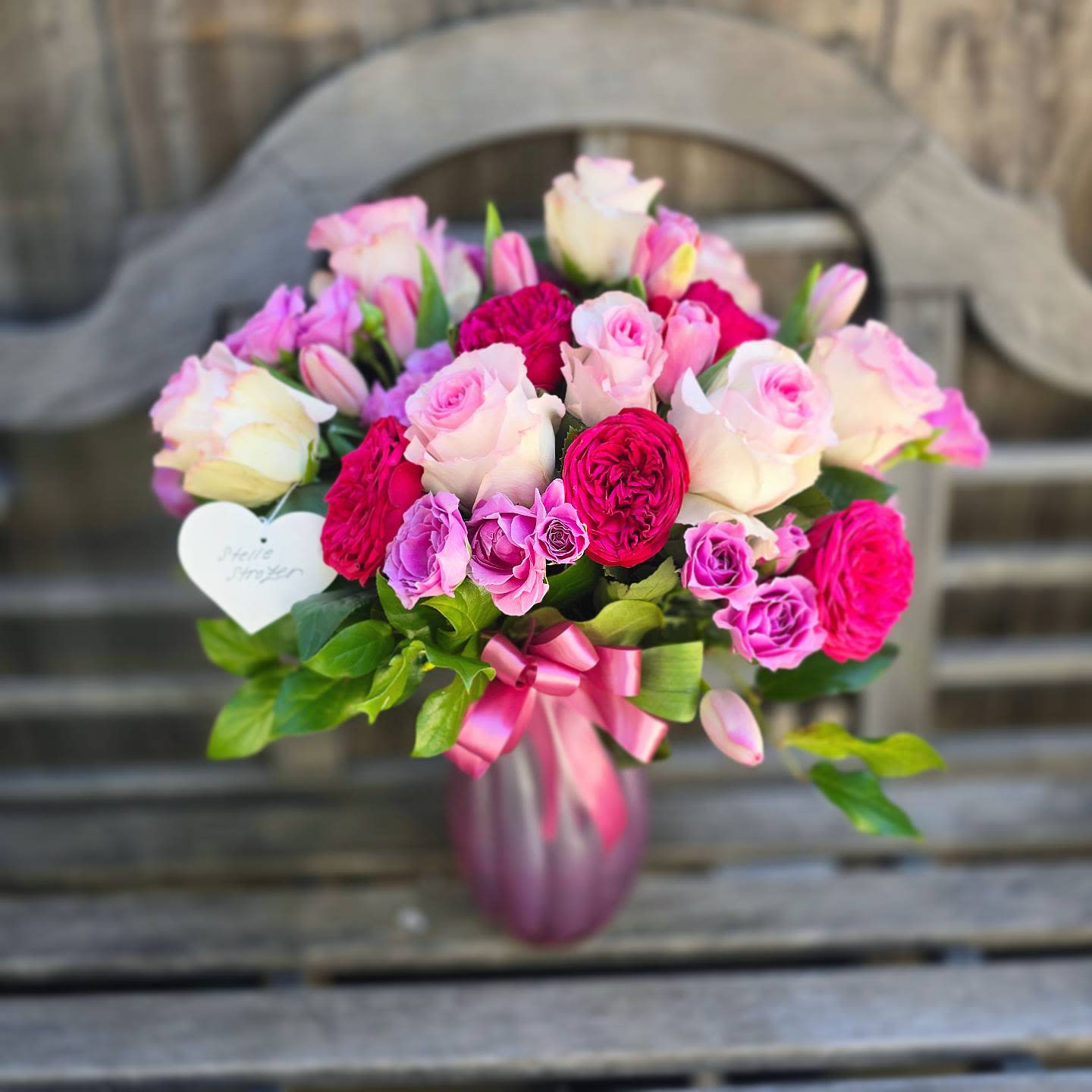 Rose Garden (Rosey Swirls) - This arrangement features various types of roses including: Ecuadorian roses, Garden roses, and Spray roses. accented with pink tulips, and supported with greens. The &quot;Rose Garden (Rosey Swirls)&quot; arrangement comes delivered in a &quot;Rosey Swirls&quot; pearlescent vase, and is adorned with a matching ribbon.  appropriate color substitutes for this item would be premium florals in shades of purple, pink, dark pink, or red. and appropriate floral substitutes would include premium florals in the following varieties: Roses, Garden Roses, Spray Roses, Peonies, Ranunculus, Tulips, lisianthus, or hydrangea. Our floral designer will take care to select the highest quality and most similar style of flowers to artfully create a beautiful arrangement for your loved one.