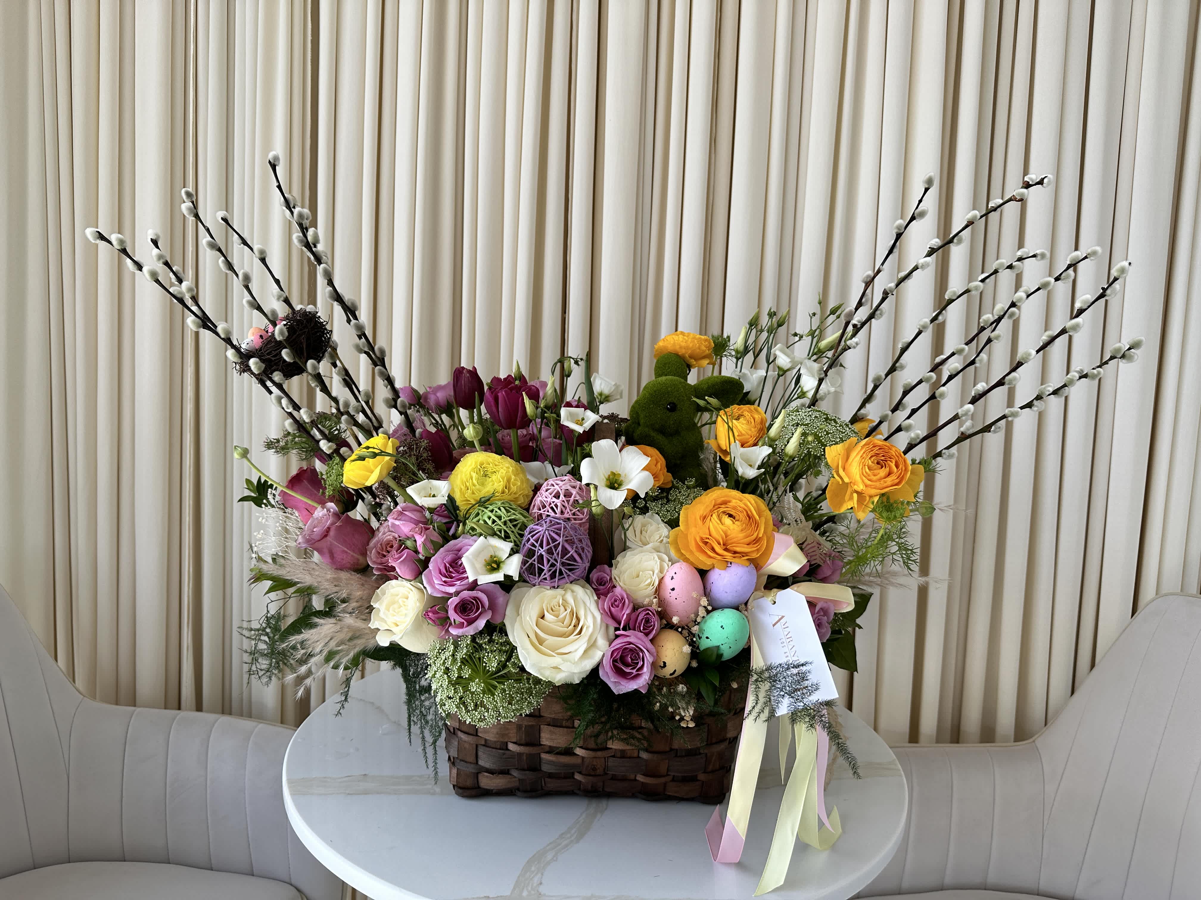 Easter Cheer  - Celebrate the joy of Easter with this delightful basket overflowing with bright and cheerful blooms, all nestled around a sweet bunny figurine in a beautiful woven basket. Perfect for brightening someone's day or as a festive centerpiece for your Easter brunch.  