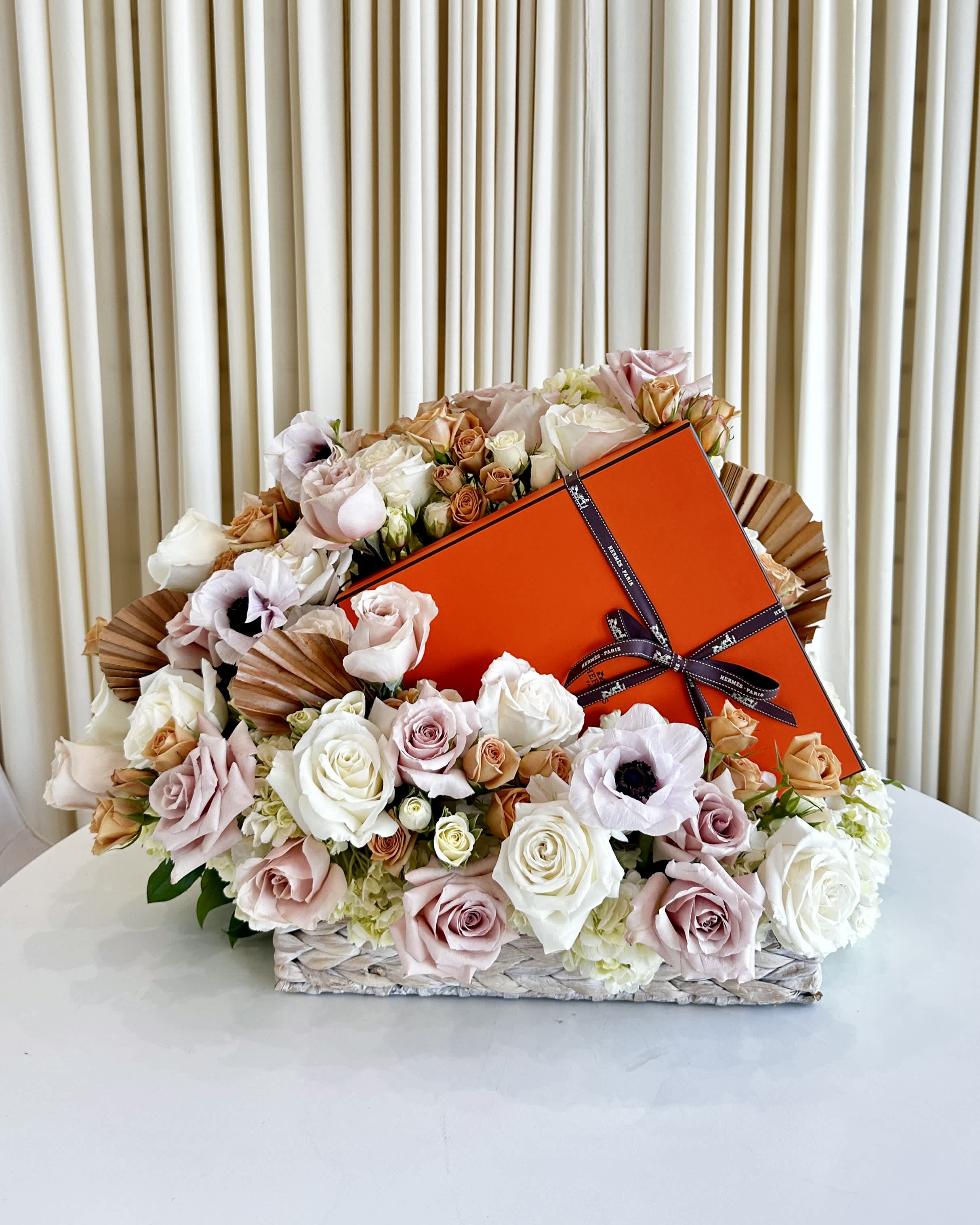 Custom Luxury Flower Arrangement - !!! Gift not included but can be provided by customer!!! Indulge in the art of gifting with our &quot;Elegance in Bloom&quot; custom luxury flower arrangement. Elevate your floral gift-giving experience by personalizing this exquisite bouquet with a special touch from your heart. This arrangement combines the timeless beauty of neutral-colored roses, anemones, and hydrangeas with captivating rust-colored accents, all meticulously handcrafted into a stunning basket weave design vase.  Each flower in this arrangement is carefully selected for its freshness and quality, ensuring a long-lasting display of natural beauty. The neutral hues provide an air of sophistication and elegance, making it a perfect choice for various occasions, from birthdays to anniversaries, weddings to corporate events, or simply to convey your heartfelt sentiments.  What sets this arrangement apart is the opportunity for you to add your own luxury gift alongside these exquisite blooms, making it a truly personalized expression of your love, appreciation, or congratulations. Whether it's a bottle of fine champagne, a box of decadent chocolates, or a sentimental piece of jewelry, your chosen gift will be seamlessly integrated into the arrangement, creating a bespoke and memorable gift for your recipient.  The &quot;Elegance in Bloom&quot; arrangement not only celebrates the beauty of nature but also the unique bond you share with your loved ones. Let this luxurious creation convey your emotions in the most elegant way possible. Order now and experience the joy of giving with a personal touch that will be cherished forever.