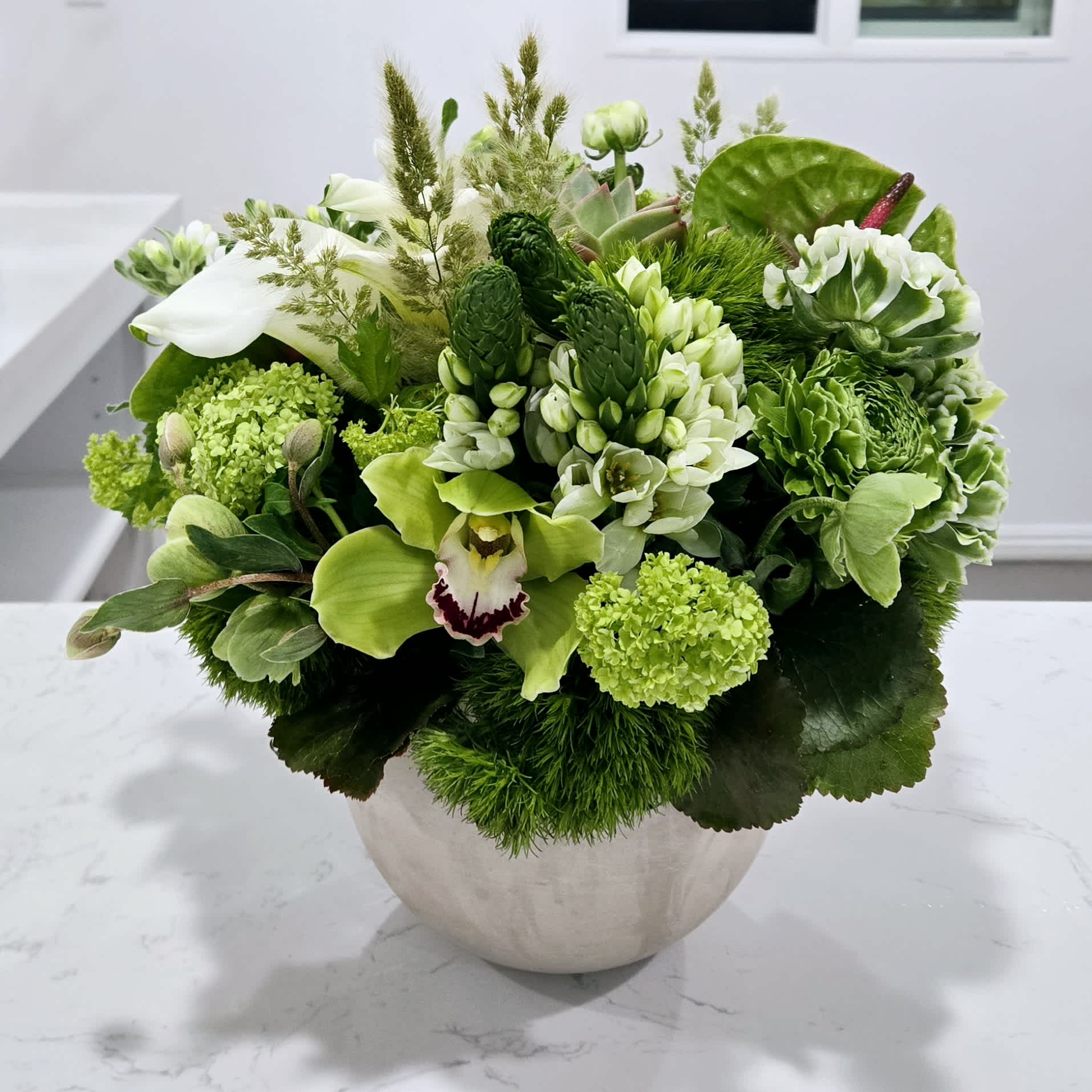 Green Vibes - An organic style arrangement with a composition of green unusual elements and a touch of premium white blooms designed in a neutral color bowl.