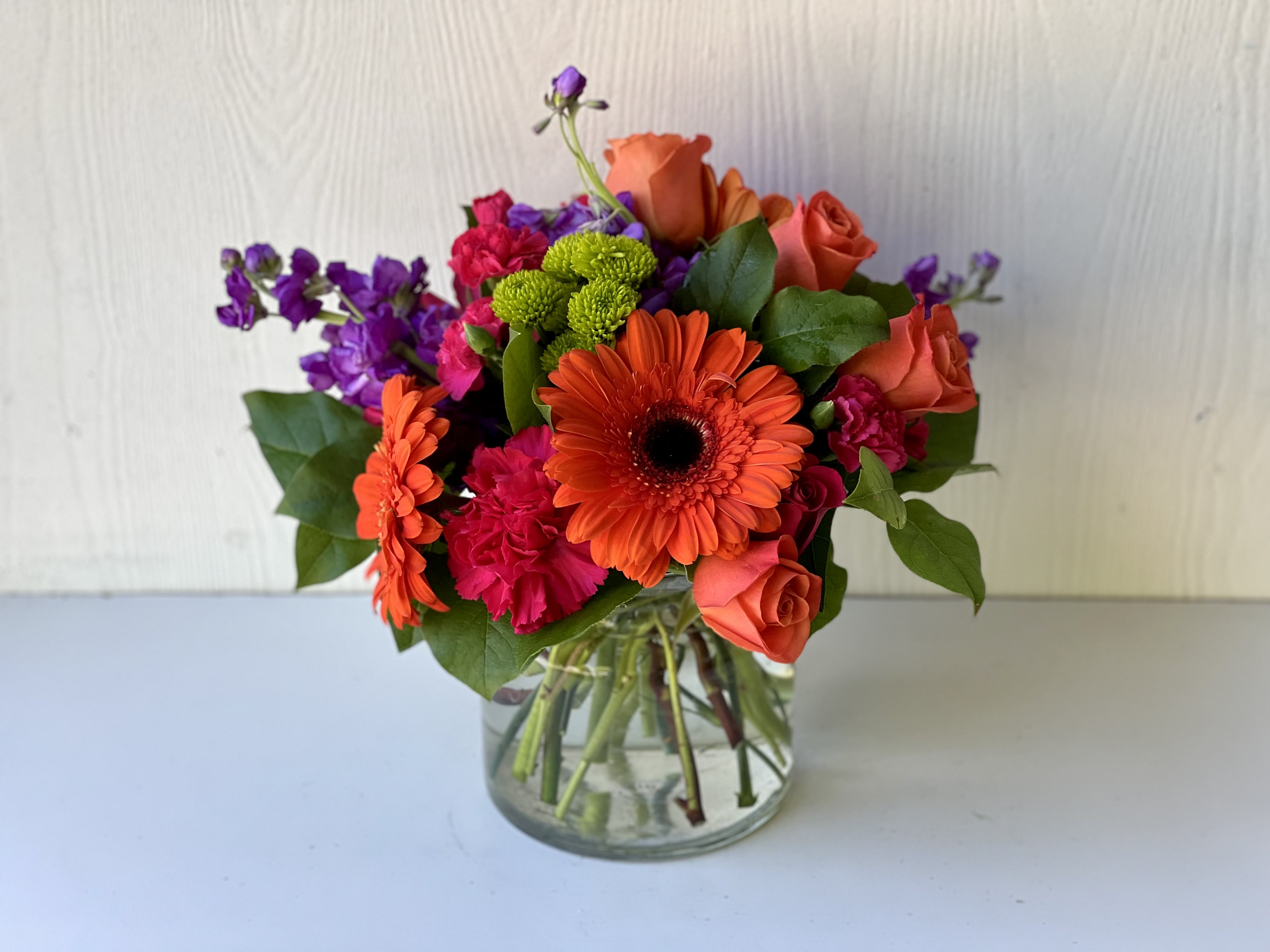 EC03 - Fiesta Bouquet - Get ready to party with the Fiesta Bouquet! This bright and cheerful arrangement is the perfect way to add some fun and color to any celebration. The joyful Fiesta Bouquet is designed with a combination of vibrant flowers of orange, pink and purple, featuring flowers such as stock, gerber daisy, roses, spray roses and carnations designed in a clear vase.  Size Pictured: Standard