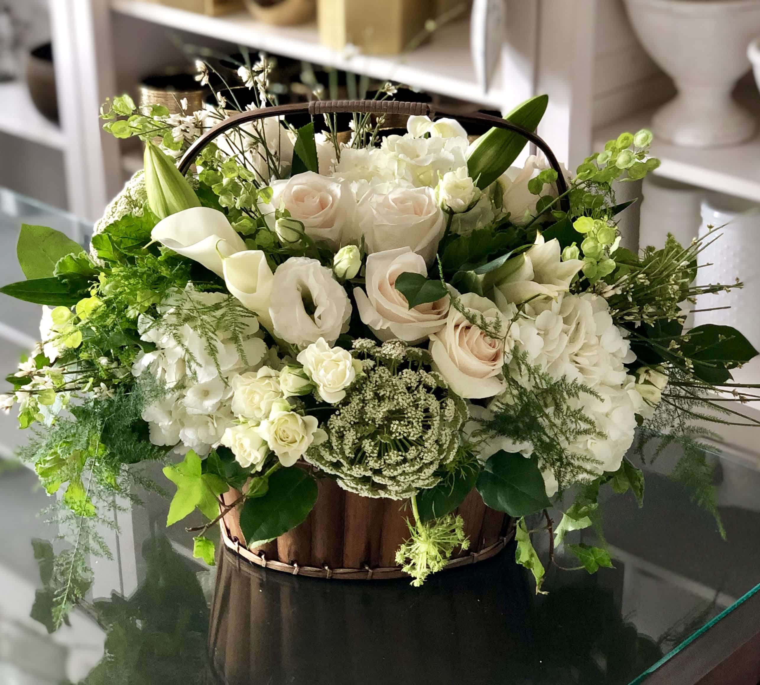 Memorable Moments - FB - Crafted with great care and consideration, this elegant basket is filled with an assortment of delicate white florals that lend an air of tranquility and solace to any space it graces. The choice of white blooms is deliberate, symbolizing purity, innocence, and the hope of a new beginning after even the darkest of times.  