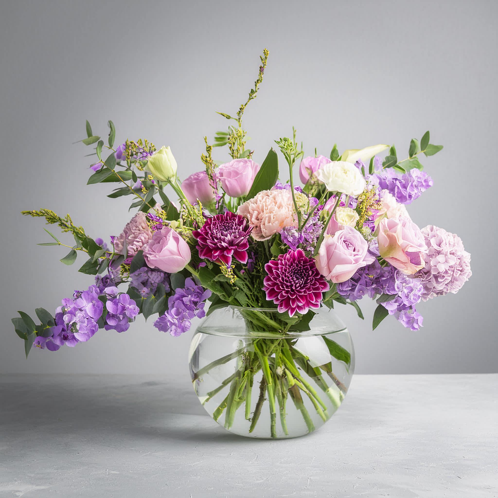 Florist Choice - Warren Street - Introducing the &quot;Warren Street,&quot; a charming bouquet inspired by the lively London thoroughfare. This arrangement is a visual symphony of vibrant purples and pinks, featuring regal dahlias, tender pink roses, and fragrant stocks. Each bloom is thoughtfully chosen for its color and texture, arranged among verdant foliage to create a striking contrast.  