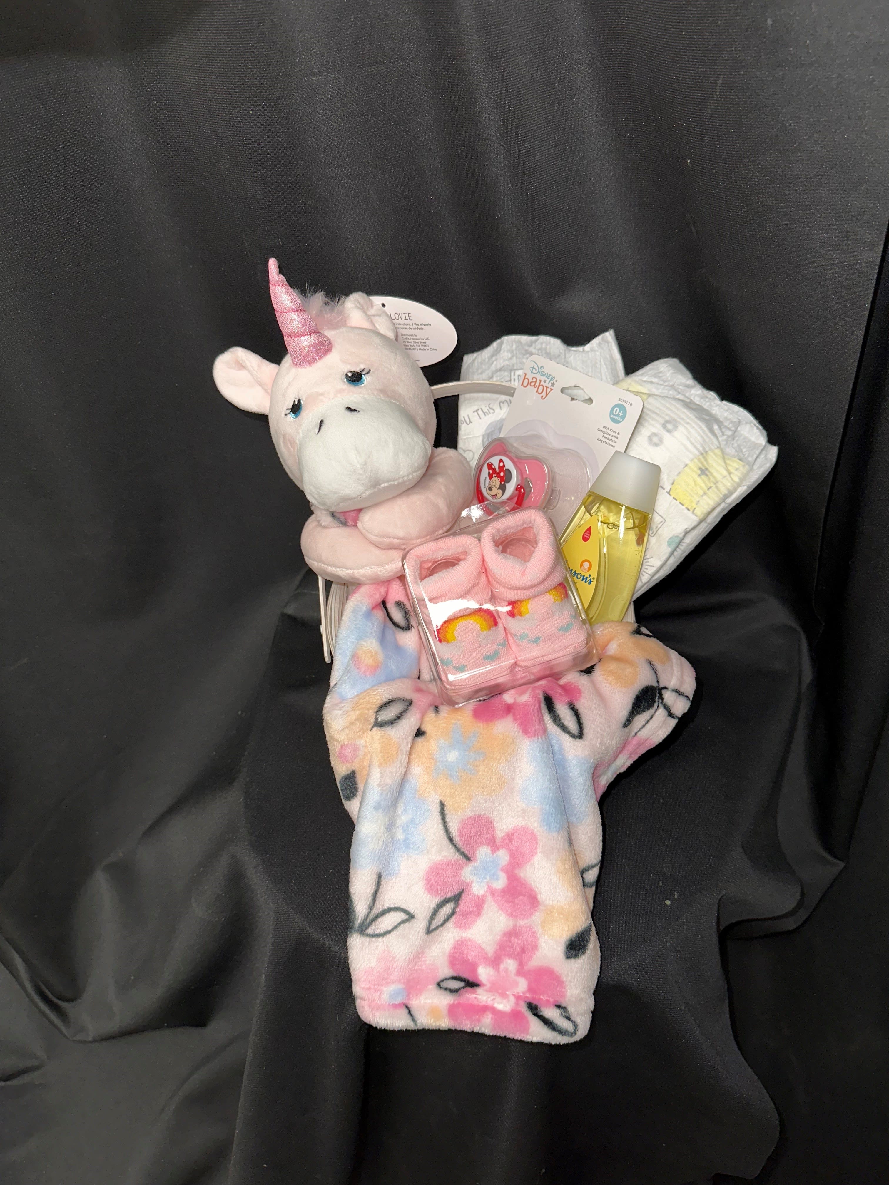 Precious Baby Girl Basket - Celebrate the joyous arrival of the precious baby girl with our charming baby essentials basket, available in two sizes to suit your needs.  Standard Size:  A sweet and cuddly stuffed unicorn with a cozy blanket Adorable pink baby socks to keep tiny feet warm Sweet-smelling Johnson &amp; Johnson baby shampoo for gentle cleansing A pink pacifier for soothing comfort Diapers for practical convenience Deluxe Size (additional items):  Fisher Price baby lotion for soft, nourished skin A soft burp cloth for mess-free feeding A bottle brush for easy cleaning Rubber duckies for bath time fun A pink pacifier for soothing comfort Diapers for practical convenience These essential items are sure to welcome the newest little princess with warmth and care, making her feel right at home.