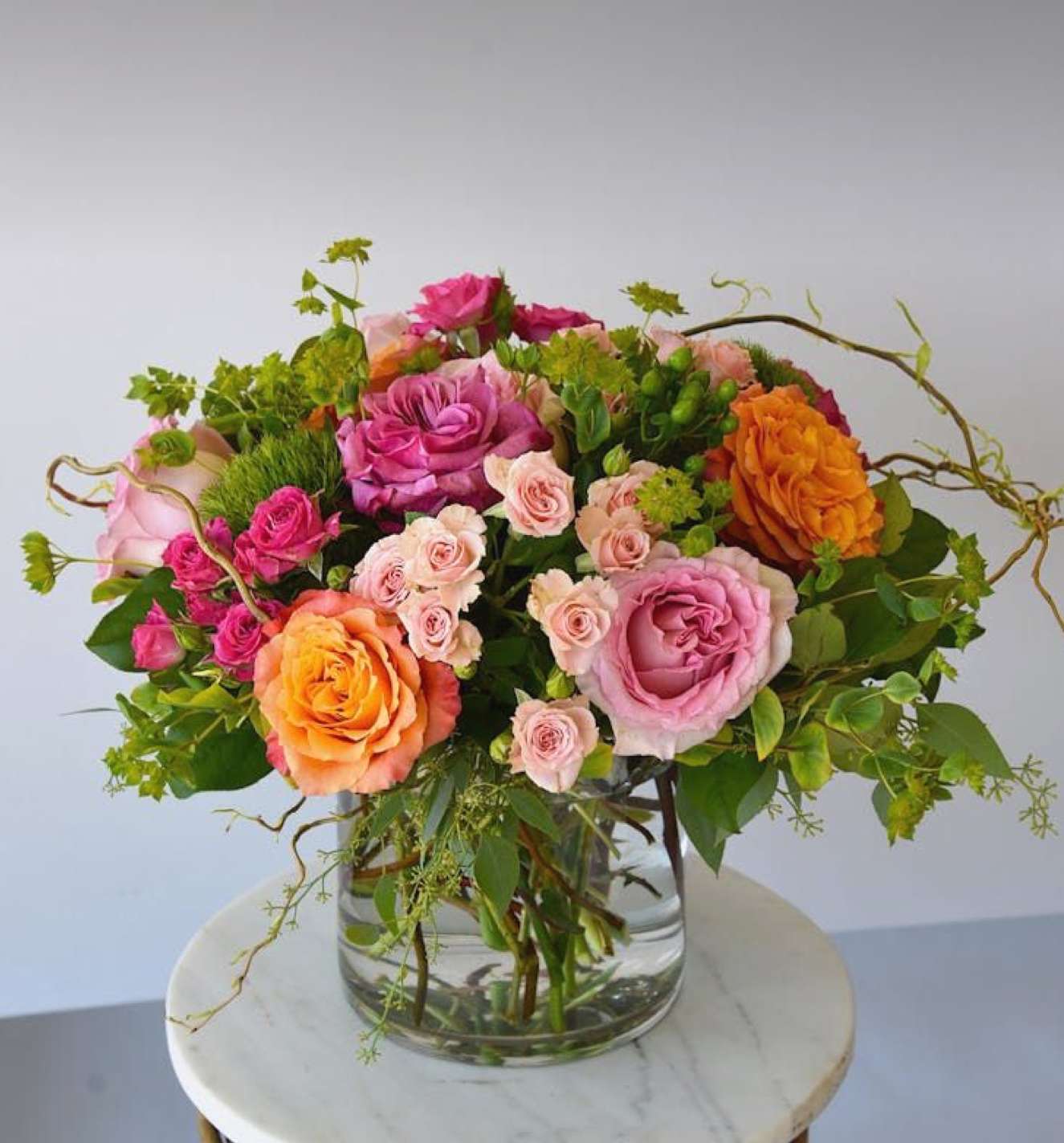 Color Me Rosy  - A lush and beautiful collection of stunning premium roses with spray roses in vibrant hues of tangerine orange, ruffled mauve-pink rose and soft pink roses.  Accented with green hydrangea, seasonal blooms and foliage designed in a classic glass vase.  Simply lovely!