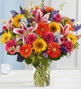 Garden Pathway - Our Garden Pathway bouquet will delight with its fresh-from-the meadow design. Hand-gathered with vibrant, fragrant blooms and lush greenery for a rich contrast of color, it’s a summertime standout that deserves to be put on display.  All-around arrangement with sunflowers, hot pink roses, pink Stargazer lilies and larkspur, blue delphinium, orange Gerbera daisies and purple statice; accented with assorted greenery Artistically designed in a clear glass cylinder vase; measures 8&quot;H arrangement measures approximately 27&quot;H x 25&quot;L We hand-design each arrangement, so colors, varieties and container may vary due to local availability Lilies may arrive in bud form and will open to full beauty in 2-3 days Sunflowers may arrive with light or dark centers