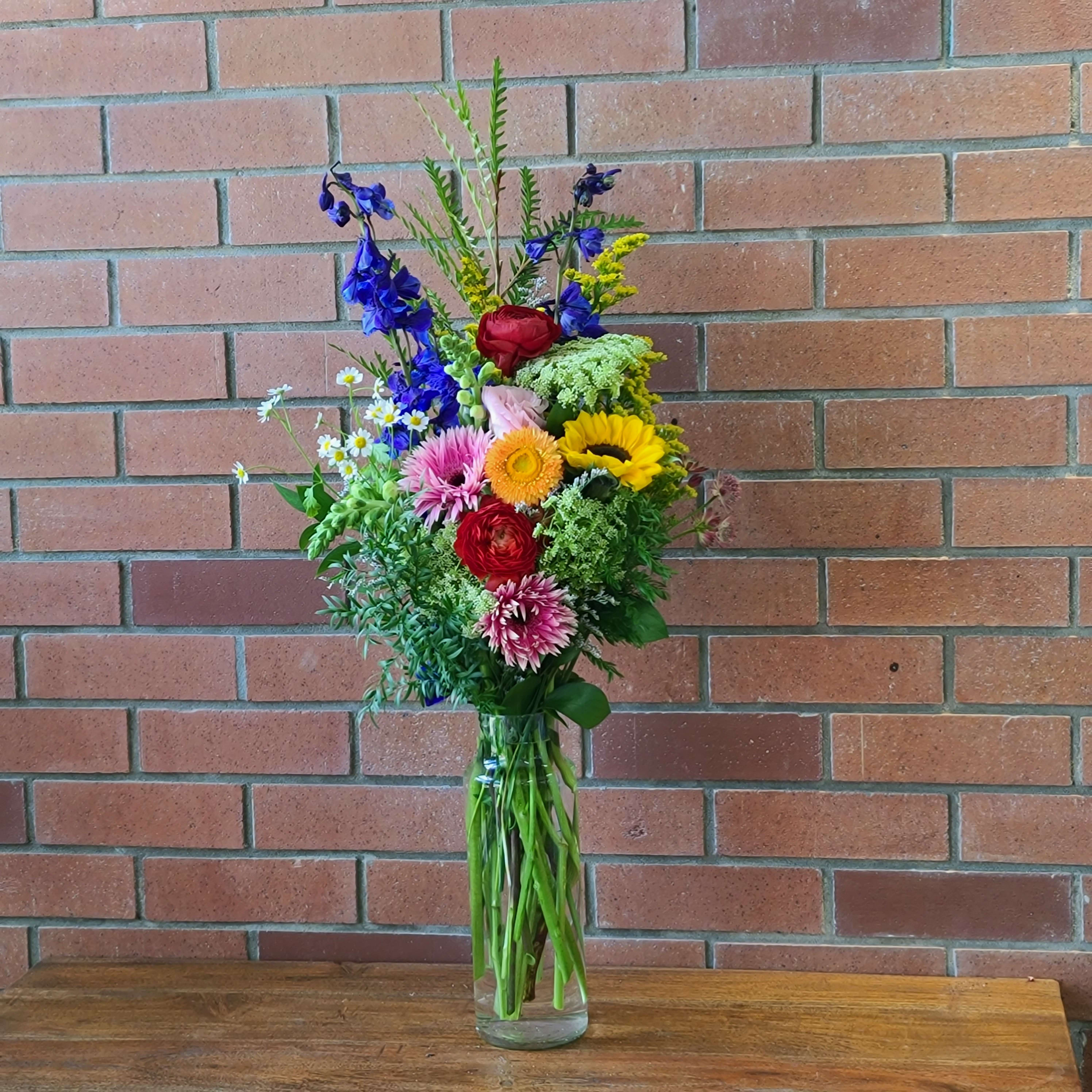 Wild Fields Bouquet - Fresh wildflower bouquet of snap dragons, blue delphinium, sunflower, caspia, ranunculus, queen anne's lace, lisianthus and more - we will use the freshest wilf flowers in house to create a farm fresh beautiful wildflower arrangement in a tall clear vase. 