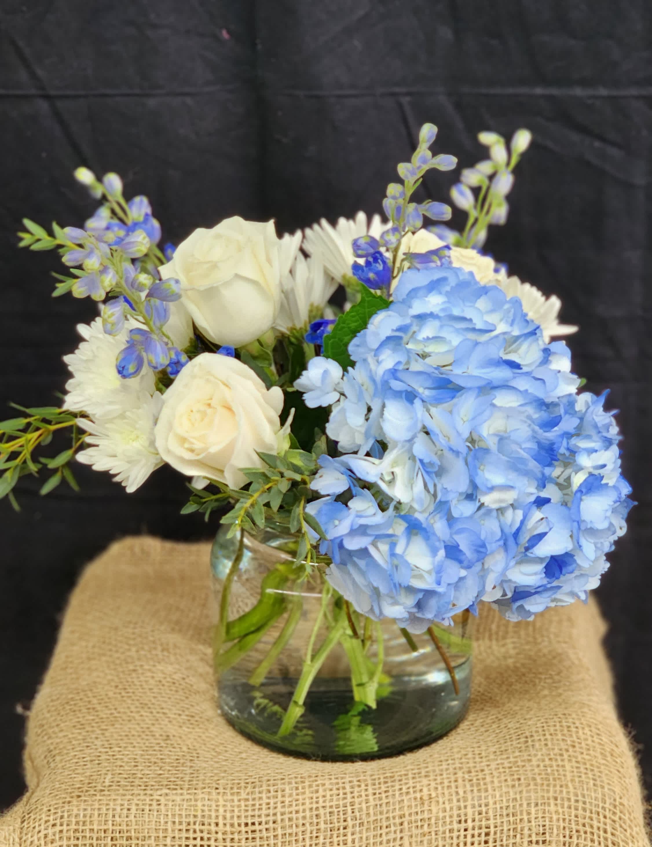 Mountain Skies - Beautiful blues contrasting against whites bring the feeling of the wonderful mountain sky. Blue delphinium, blue hydrangea, white roses and daisies make up this elegant arrangement. 
