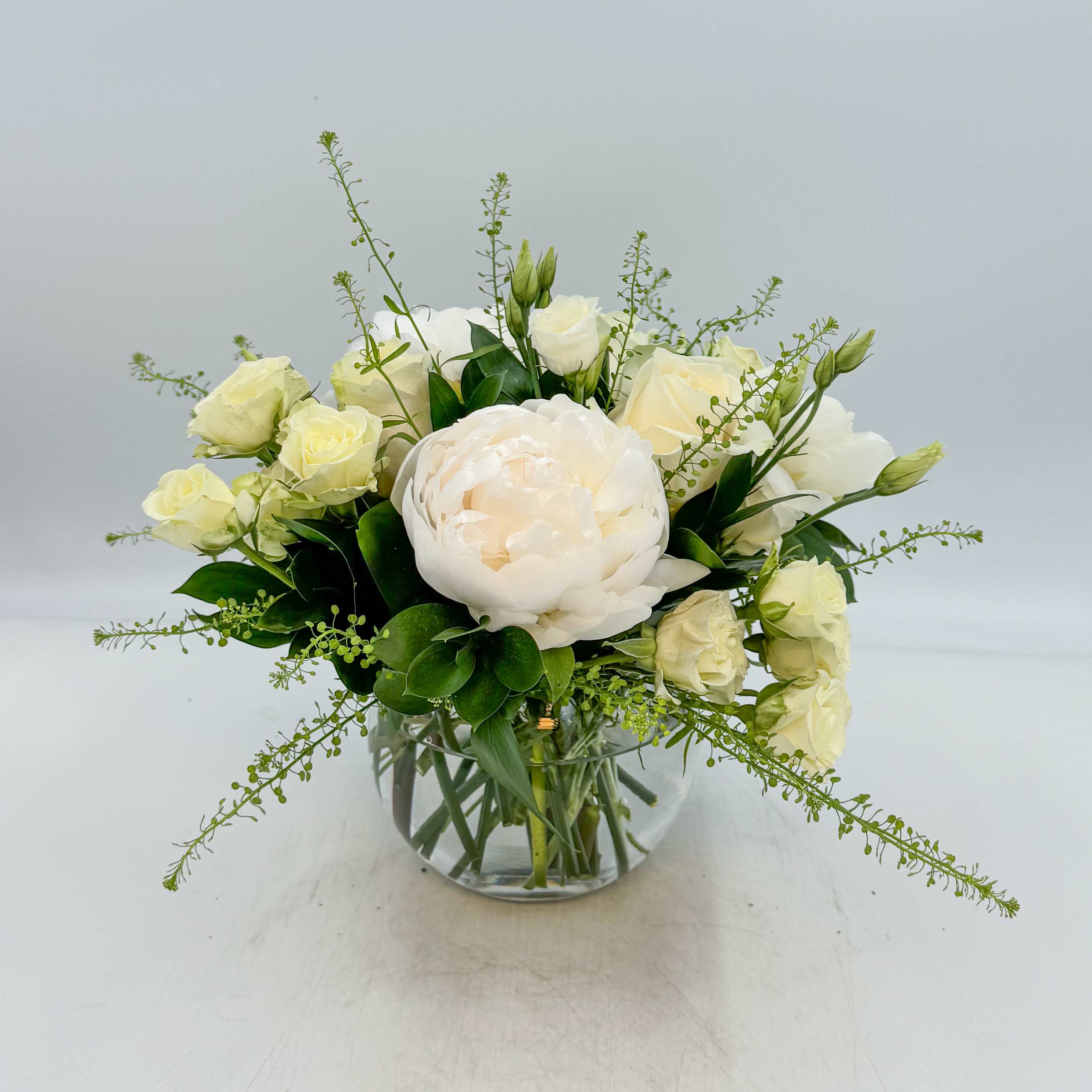 Mumzy - Mumzy features White Peonies, Cream colored Vendela Roses, White Spray Roses and White Lisianthus, Italian Ruscus and Pennygrass. Measurements: The Standard Mumzy is designed in a 6 inch glass bubble bowl vase; the Deluxe Mumzy is designed in a 8 inch glass bubble bowl vase; and the Premium Mumzy is designed in a 10 inch glass bubble bowl vase.