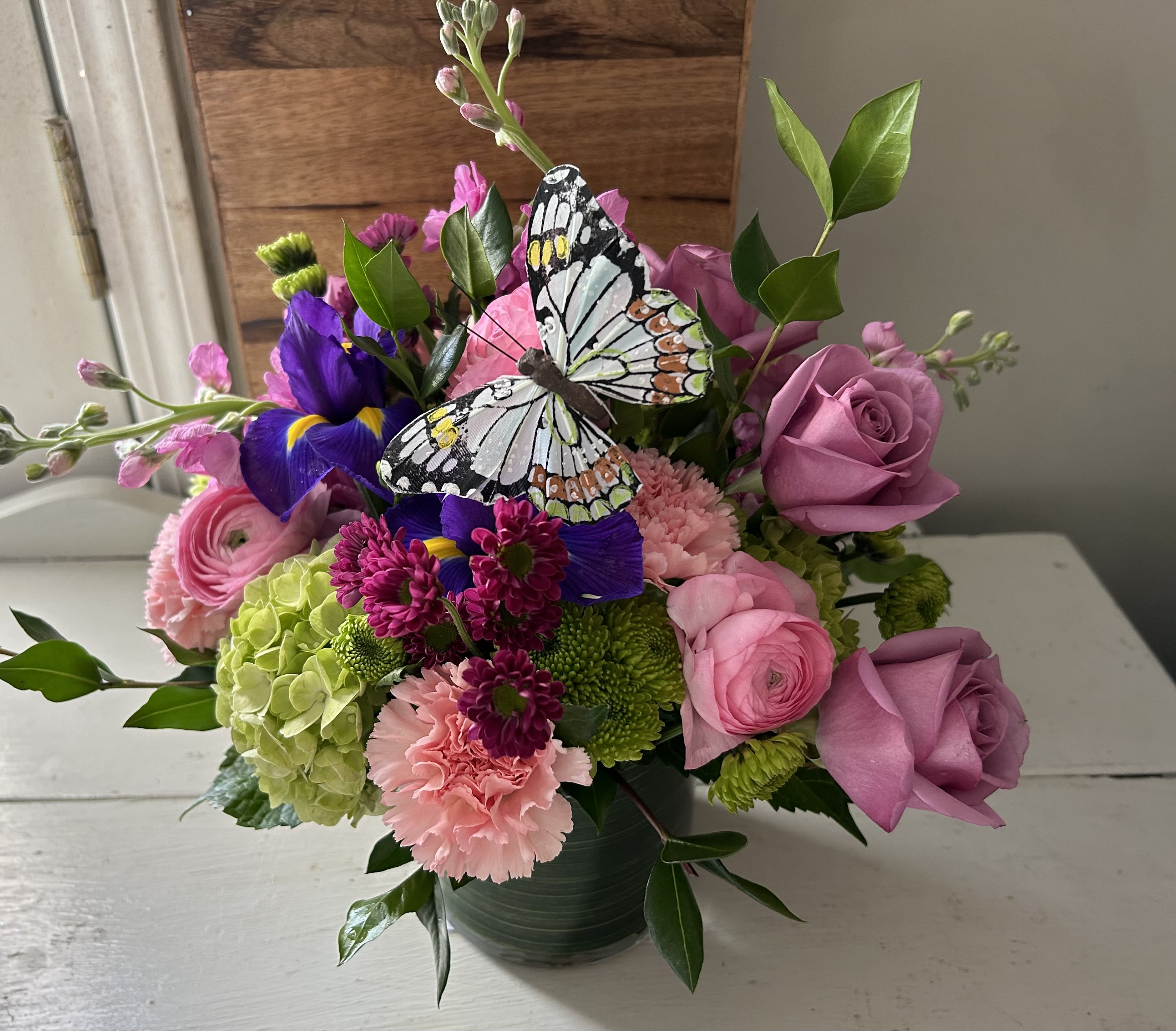 Flora Bella Summer  - A beautiful combination of green hydrangea, pink ranunculus, lavender roses, stock, purple irises, micro poms and carnations in a clear cylinder.