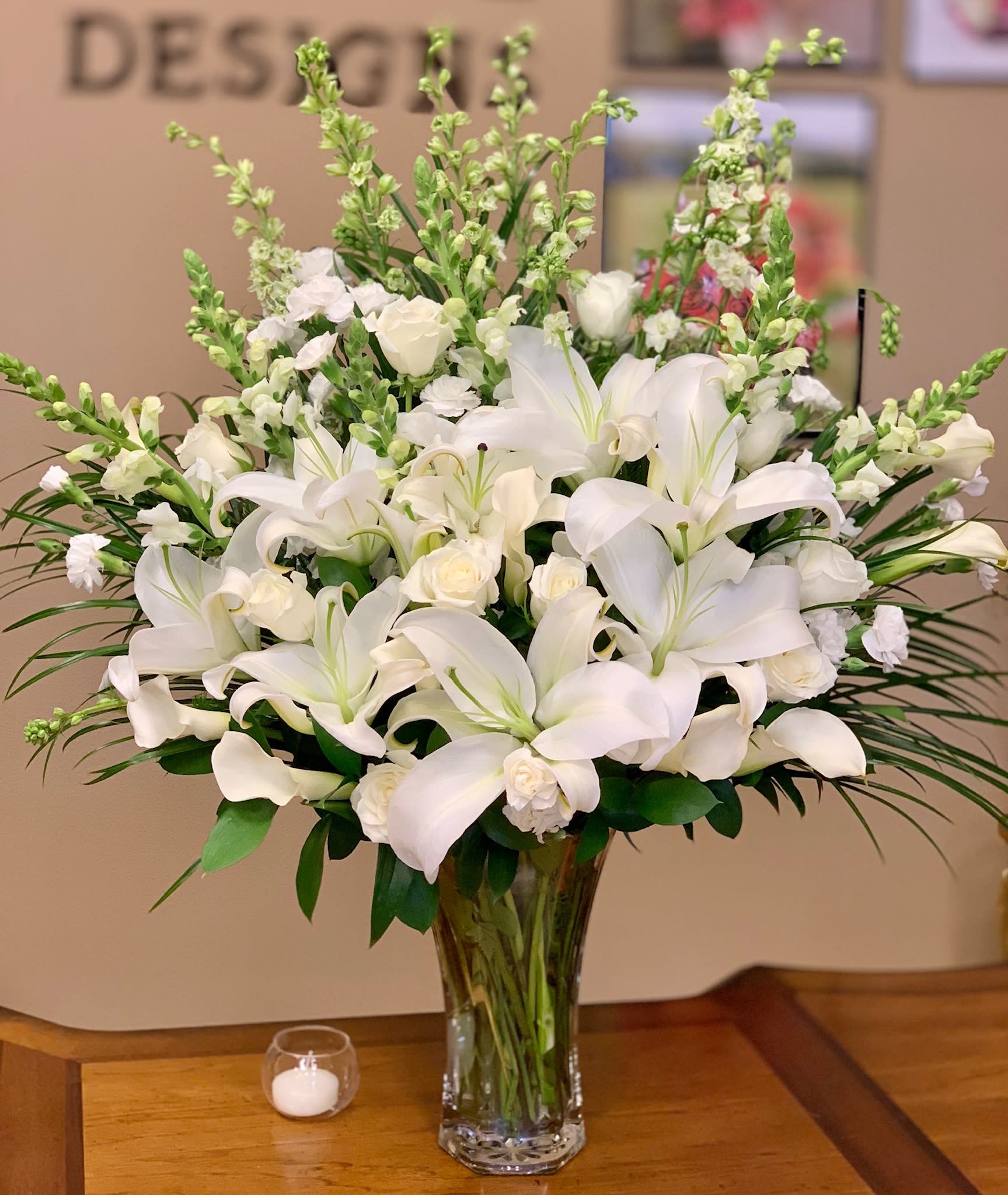 Happy in Spring - Our exclusive arrangement features a pure white floral mix blooms of white lilies, white roses, white larkspur, white mini calla lilies, white alstromeria, filler and greens. Picture shows the PREMIUM OPTION (LARGE)