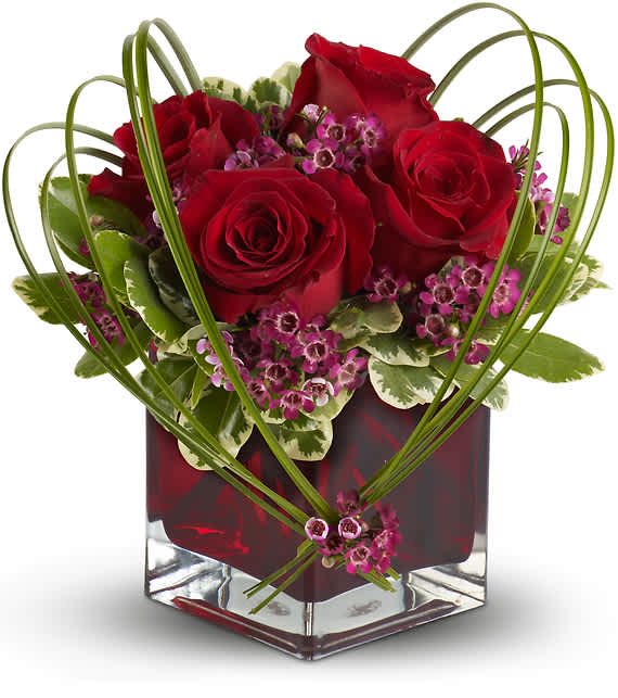 SWEET THOUGHTS BOUQUET WITH RED ROSES - A graceful heart of bear grass... tied with purple waxflower blossoms... forms a heart that appears to float above the velvety red roses in this delightful bouquet, arranged in a ruby-red cube vase. Send this beautiful floral arrangement to someone you love, and they'll think sweet thoughts about you!  Red roses and purple waxflower accented with variegated pittosporum and bear grass arrive in a red glass cube vase.  