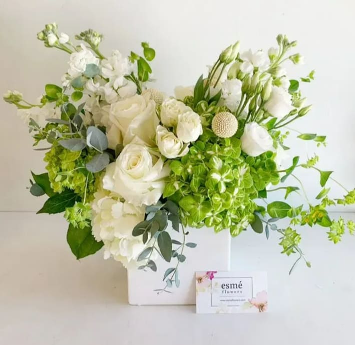 Cosima - An elegant all-white arrangement featuring a symphony of delicate ivory roses, lush green hydrangeas, crisp white lisianthus, and seasonal premium blooms. This arrangement is perfect for any occasion or as a stunning statement piece in any setting.