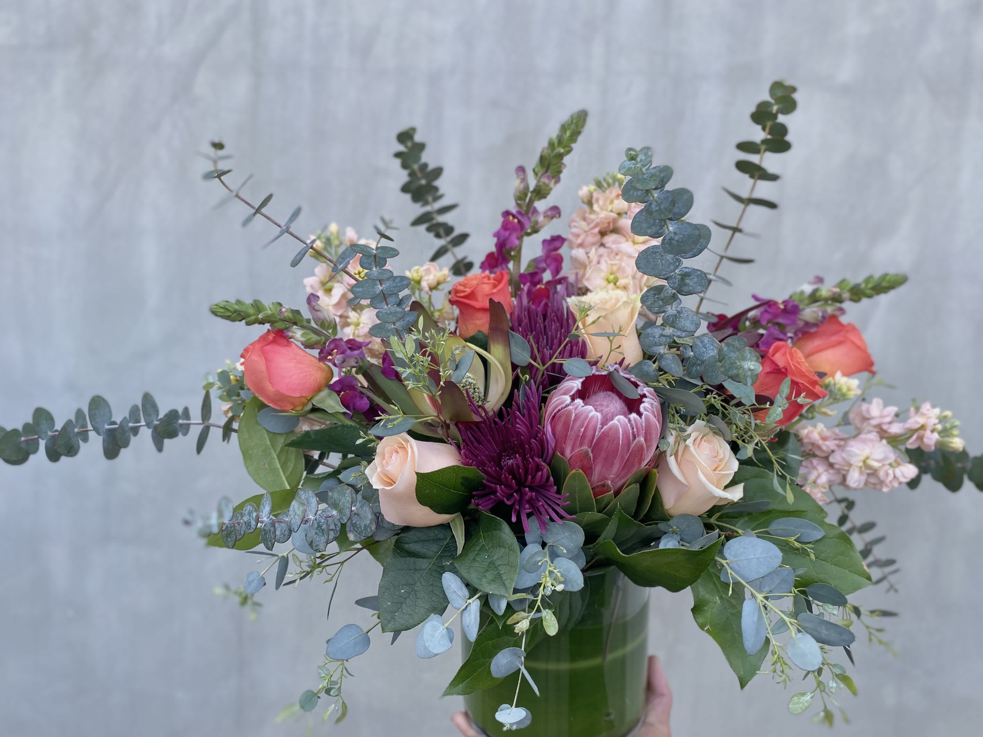Deep, Dark, and Delightful Deep, Dark, and Delightful - This stunning arrangement includes proteas, stock, snapdragons, roses, safari, and eucalyptus arranged in a glass vase.