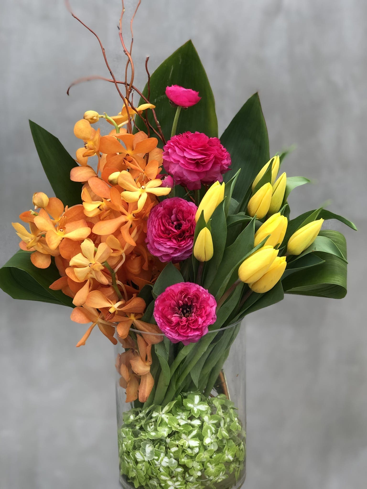 Sunday Brunch  - Beautiful orange orchids, pink roses and yellow tulips arranged in a glass cylinder vase, bright and colorful.