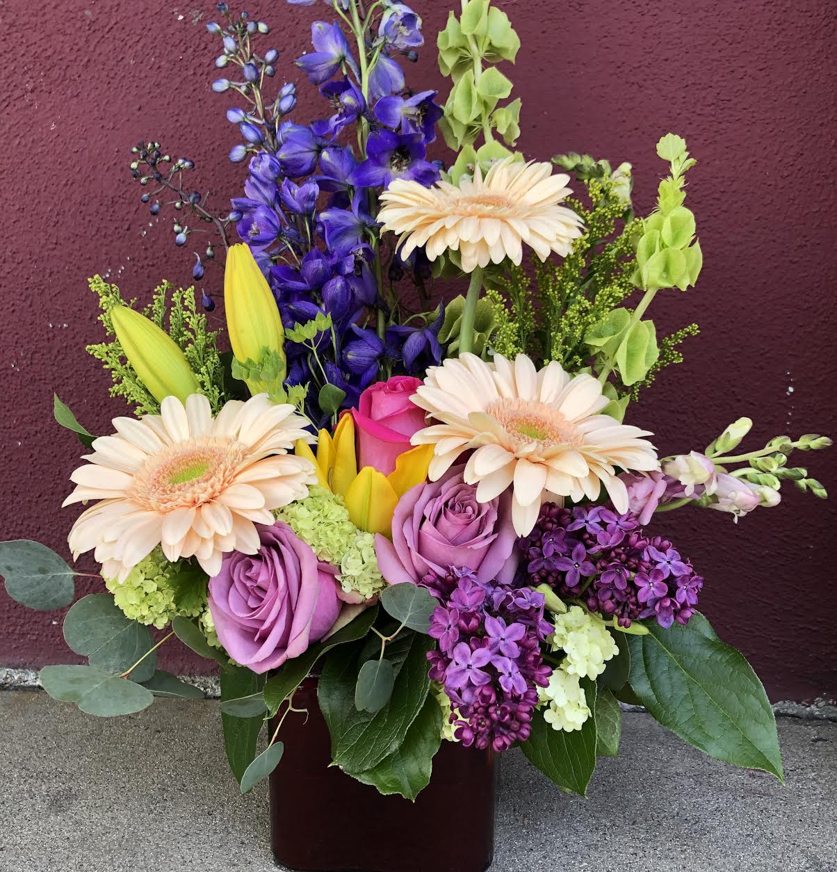 You Are Beautiful You Are Beautiful - GERBERA, BLUE DELPHINUM, STOCKS,BELLS OF IRELAND LILYS AND ROSES IN GLASS VASE.